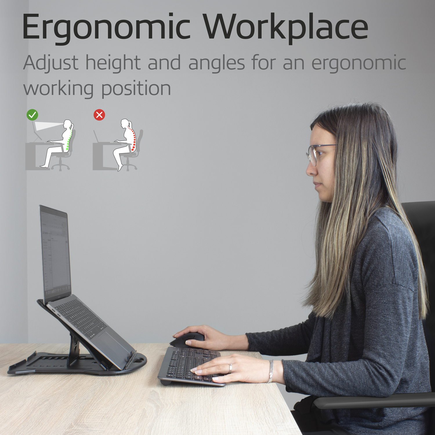 A woman sitting at a desk with a laptop. There is an ergonomic laptop stand.