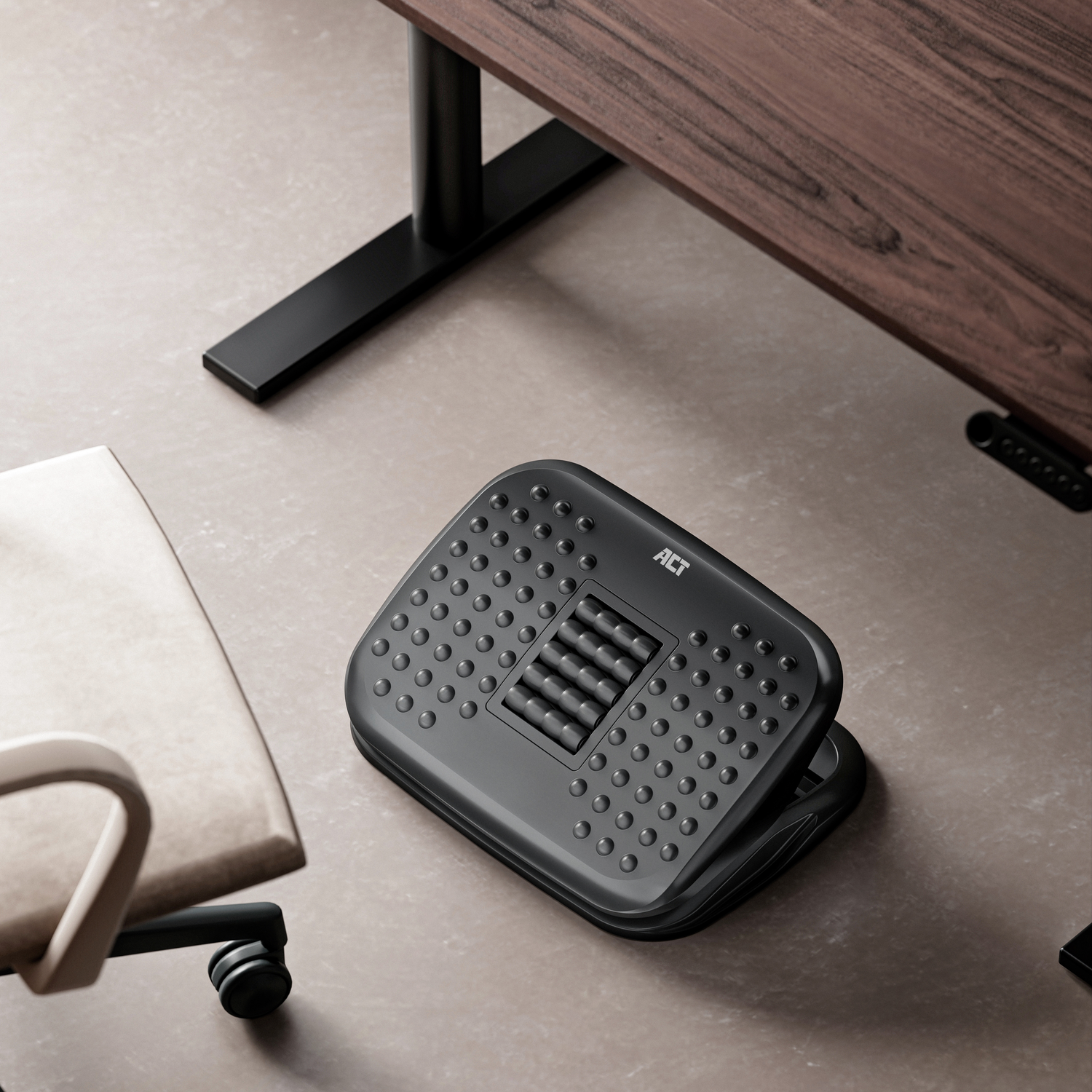A black footrest under a wooden desk, with a chair in the background. The footrest has many bumps.