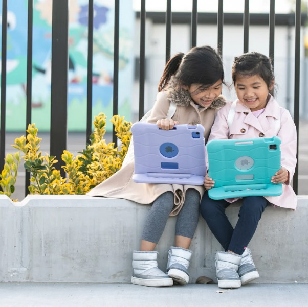 Beton bir çıkıntı üzerinde oturan ve tablet tutan iki genç kız. Gülümseyerek, dışarıda.