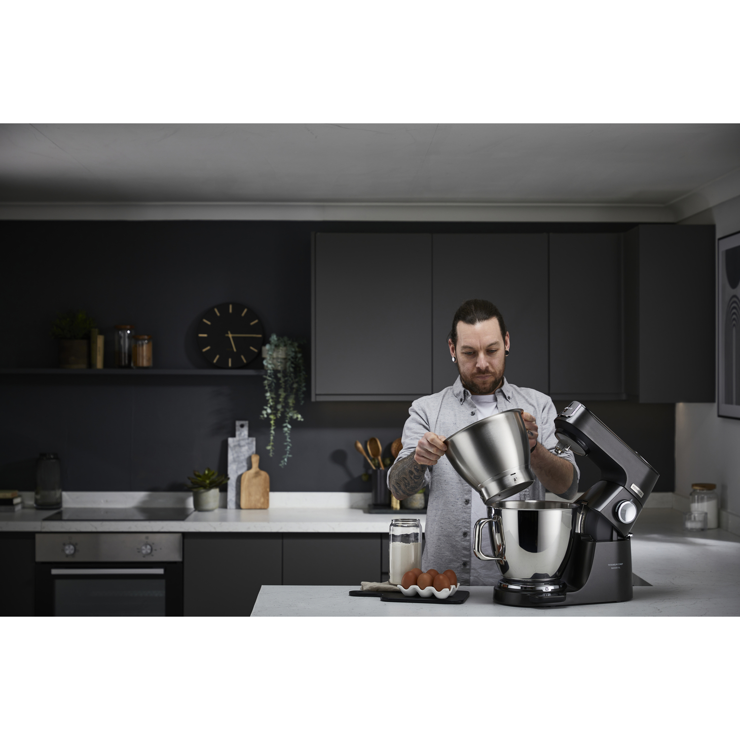 Un homme ajoute un bol à un mélangeur Kenwood noir dans une cuisine moderne.