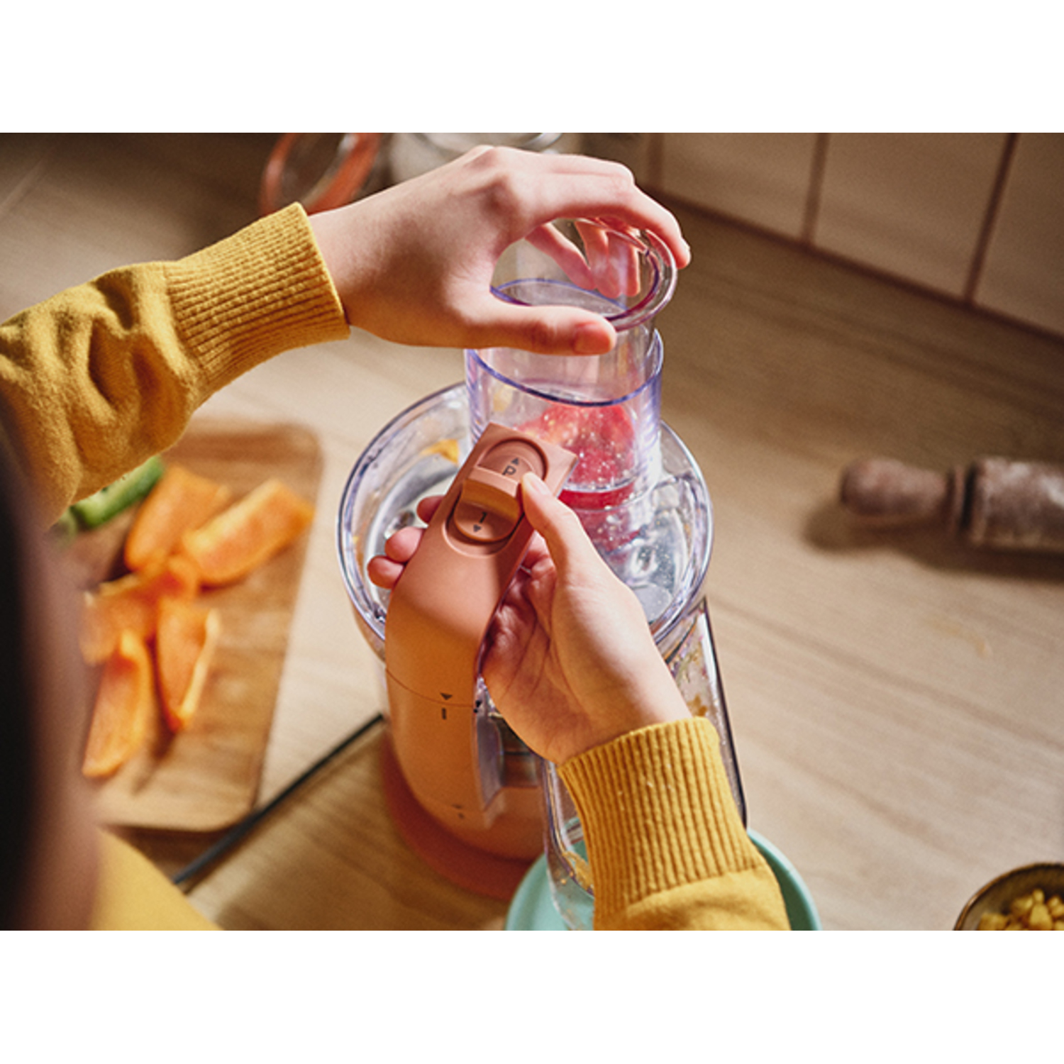 Mains utilisant un robot culinaire. Le robot est orange et contient des aliments hachés.