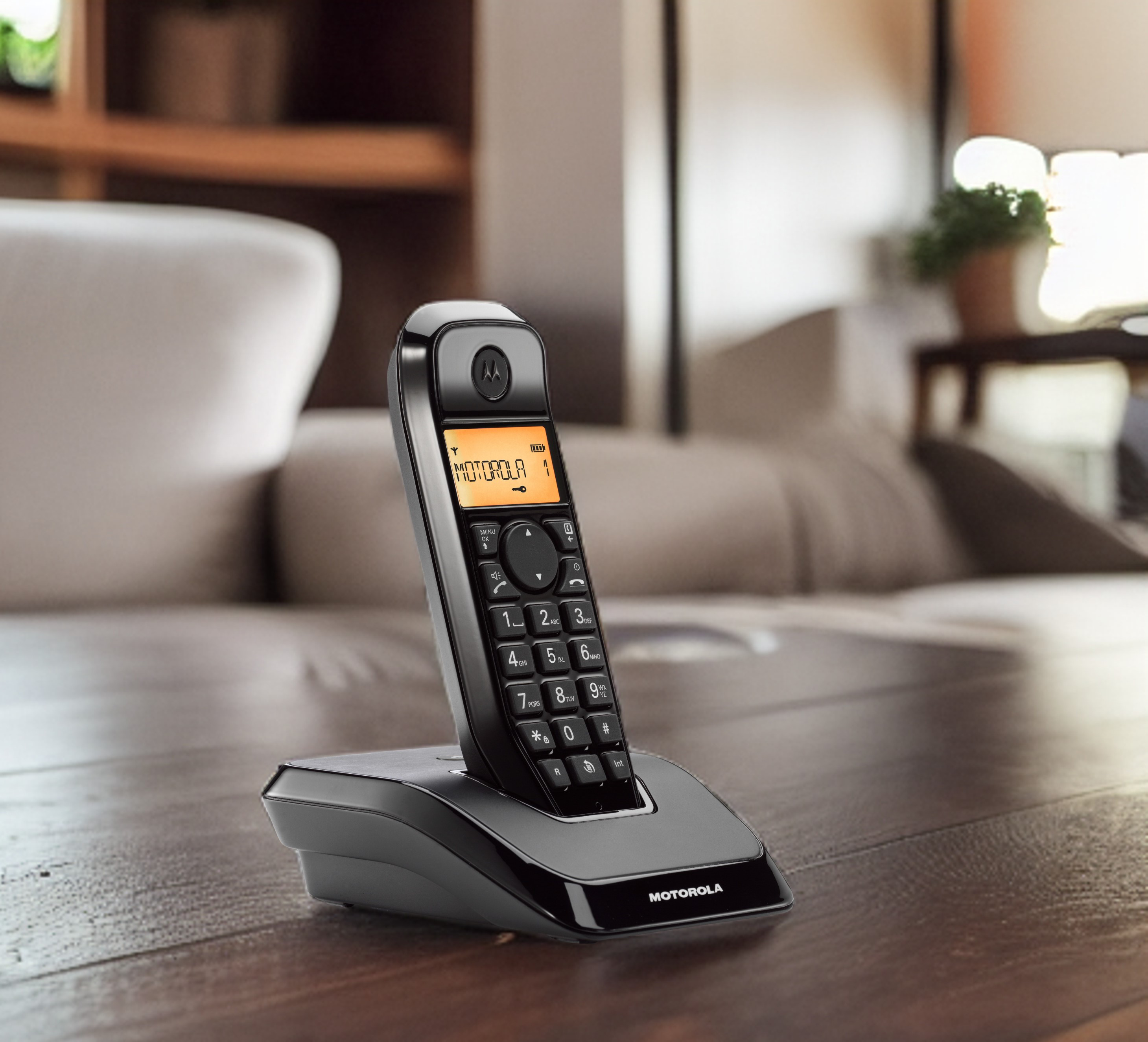 Fekete Motorola telefon a tartóján, szöveges képernyővel. Fa asztal, homályos háttér.
