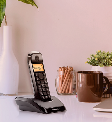 Fekete vezeték nélküli telefon töltőállomáson, ceruzákkal, bögrével és növénnyel.