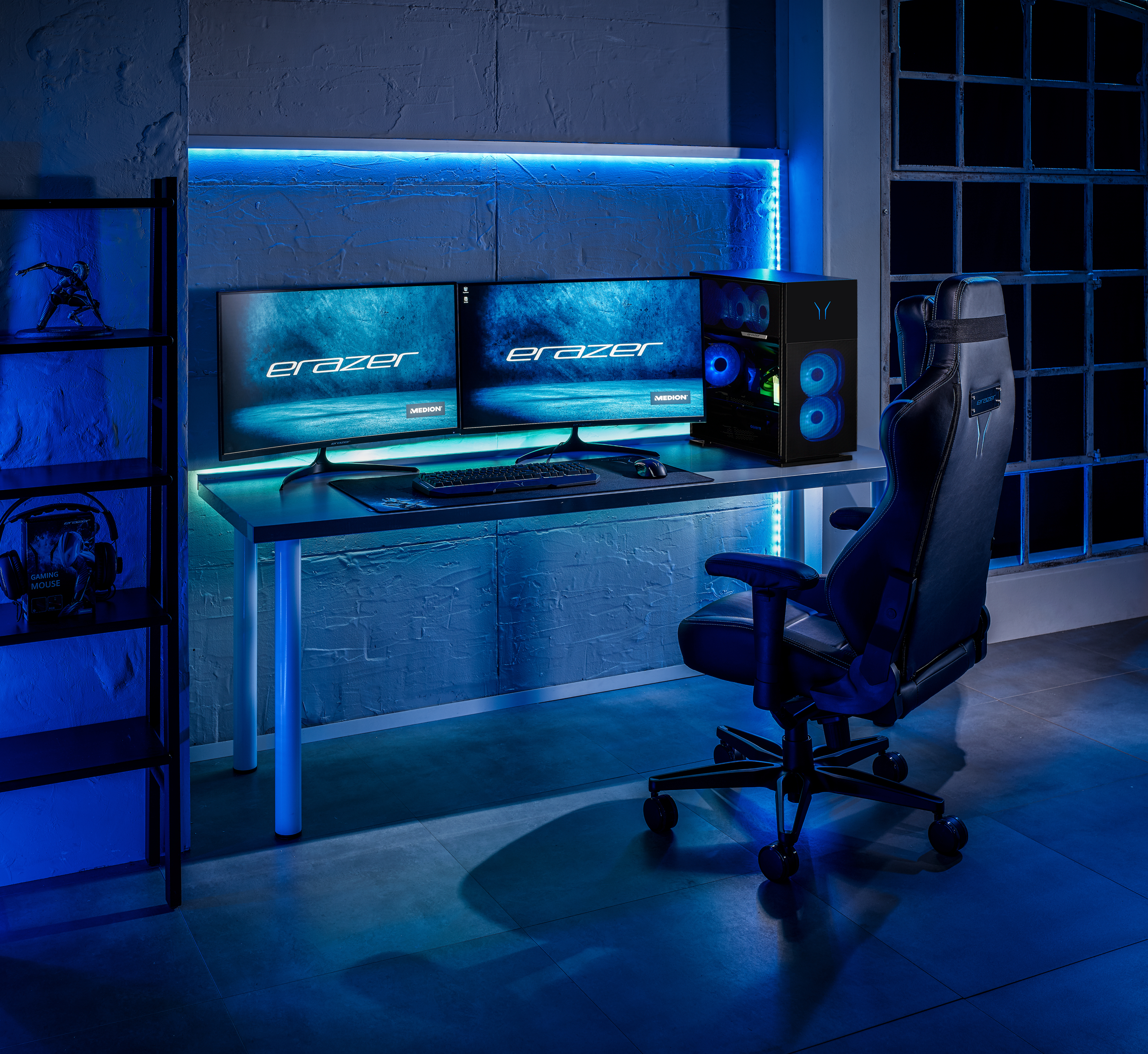 Un'impostazione di gioco con due monitor, un computer, una sedia e scaffali.