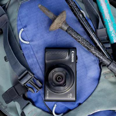 Eine schwarze Canon-Kamera mit Objektiv liegt auf einem Rucksack mit Trekkingstöcken.