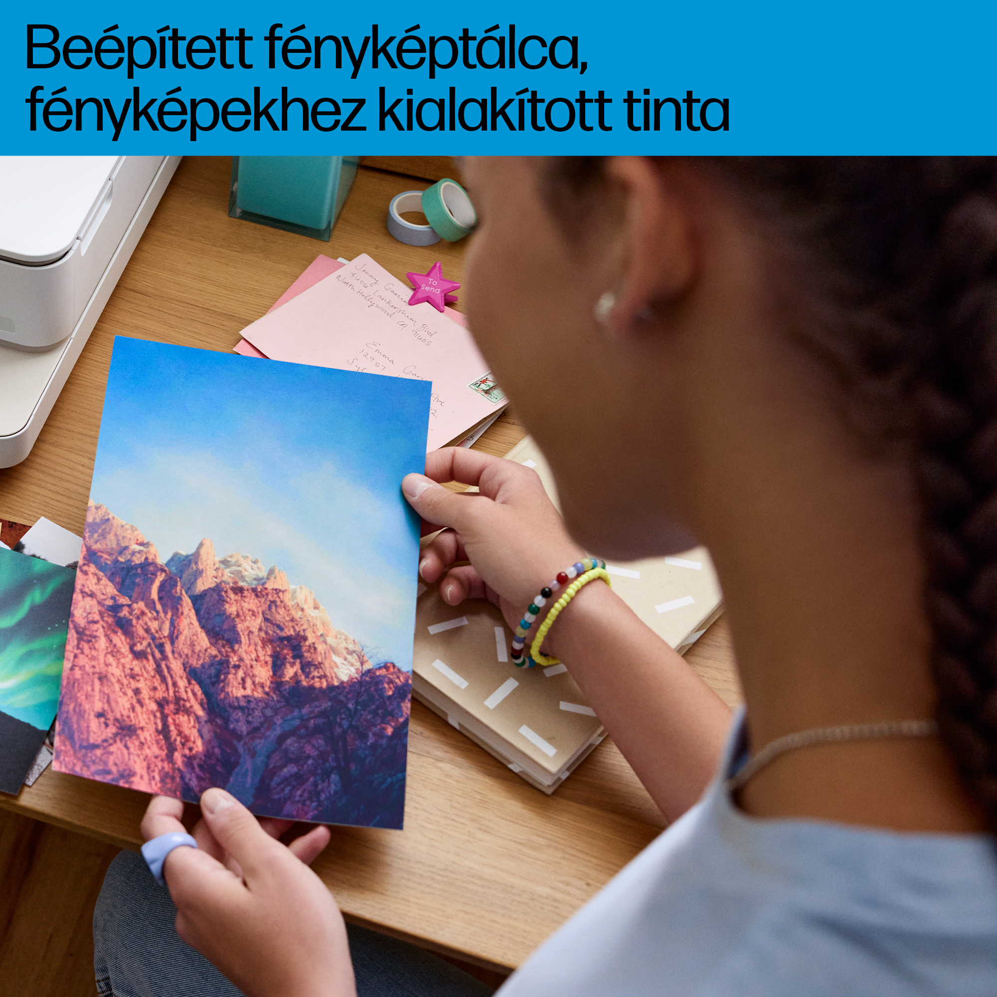Egy személy egy hegyvidéki tájról készült fotót tart, más fotókkal és jegyzetfüzetekkel.