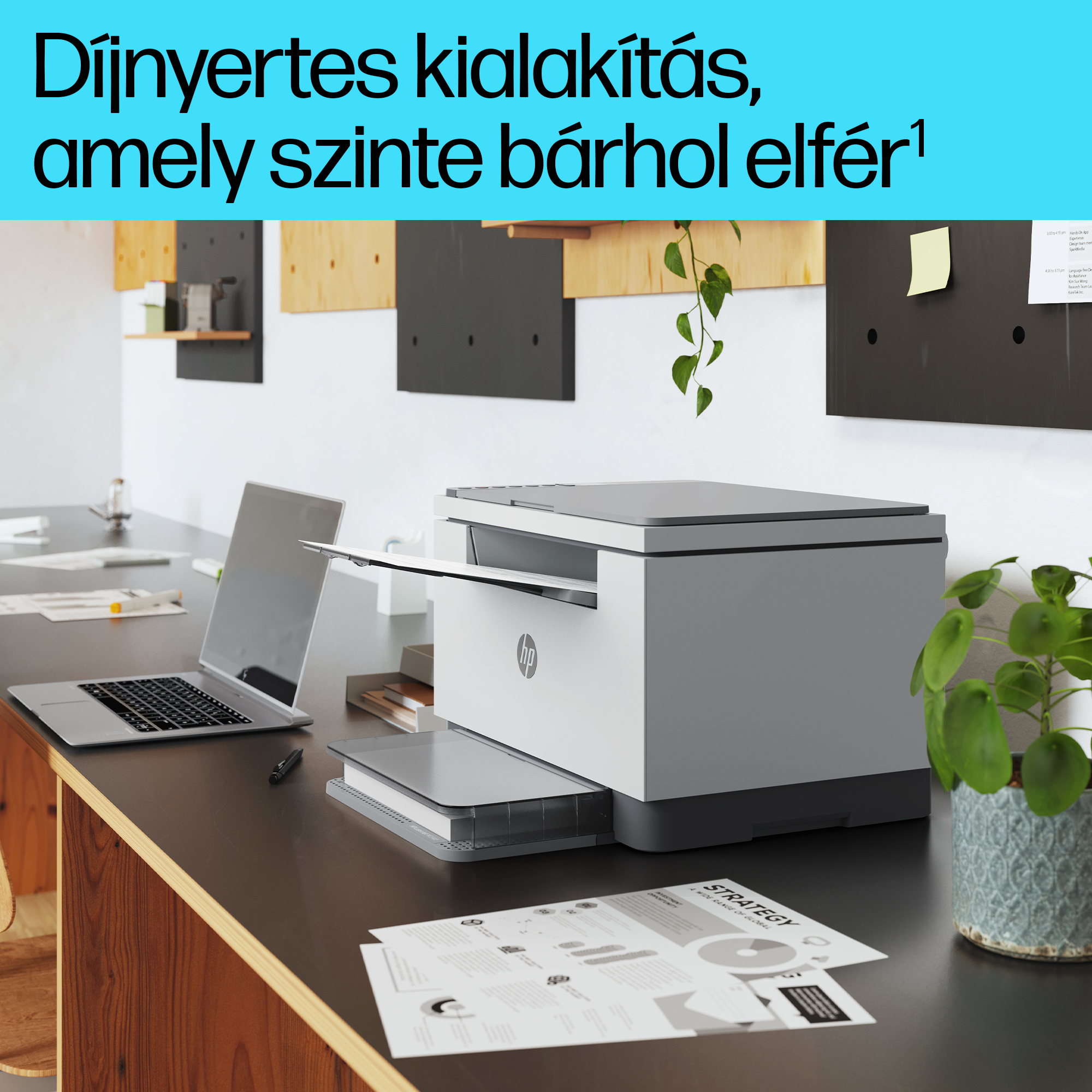 Nyitott tálcás nyomtató az asztalon, laptop, papírok és növény.