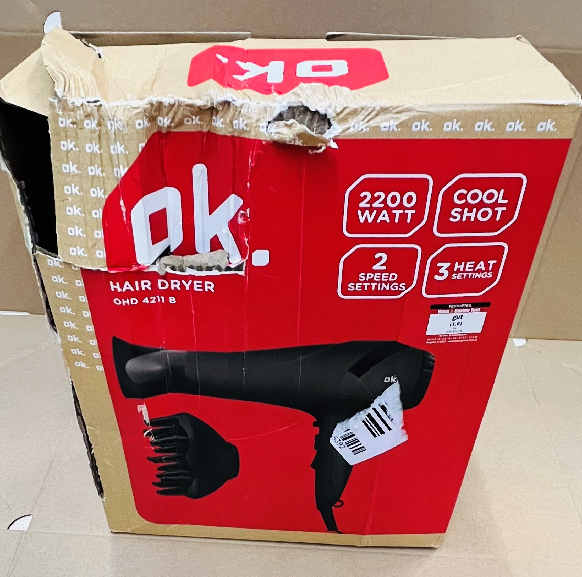 Uszkodzone kartonowe pudełko. Z przodu widnieje marka "ok." i szczegóły suszarki do włosów.