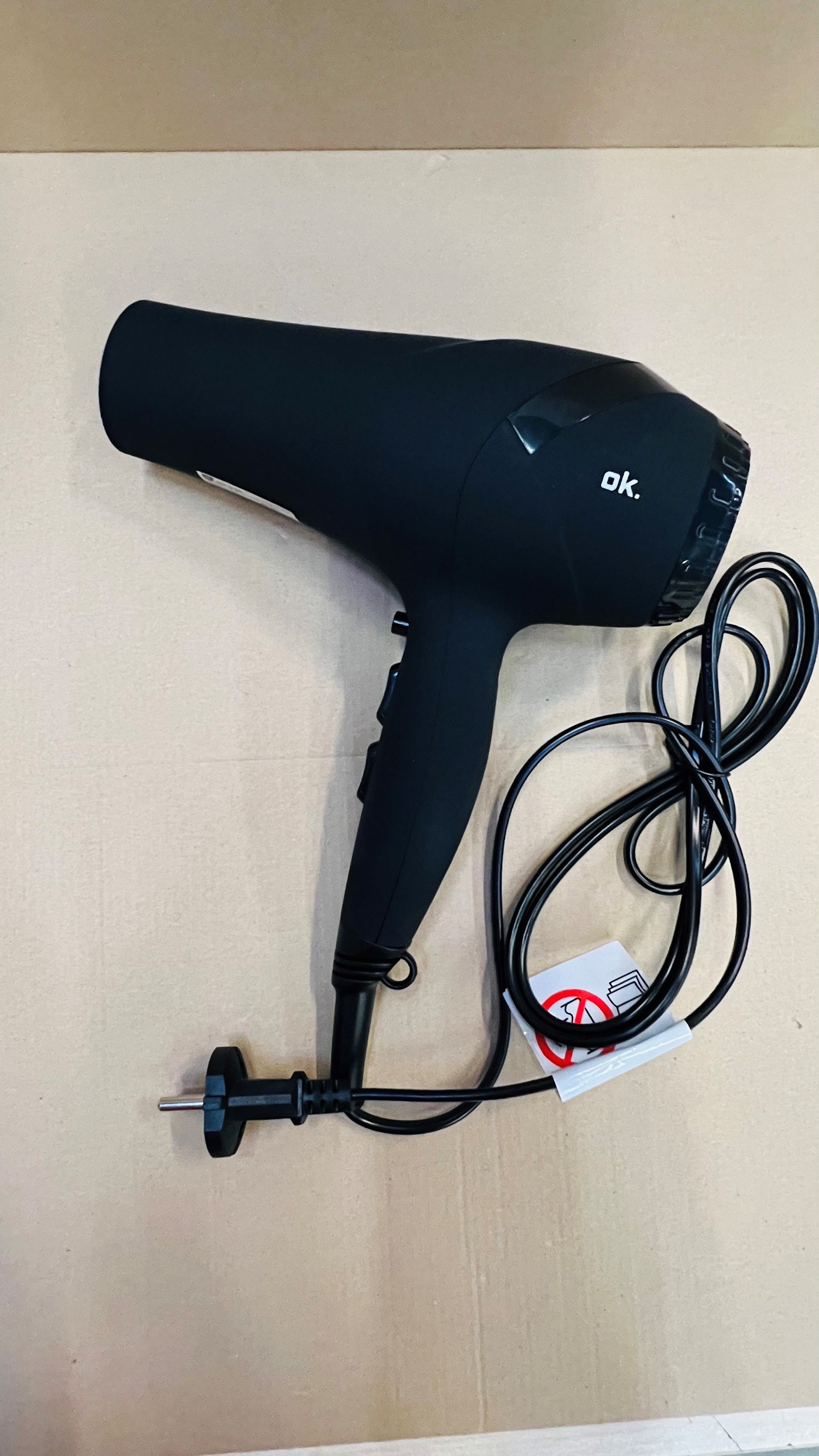 Czarna suszarka do włosów na brązowej powierzchni. Przewód jest zwinięty z boku.