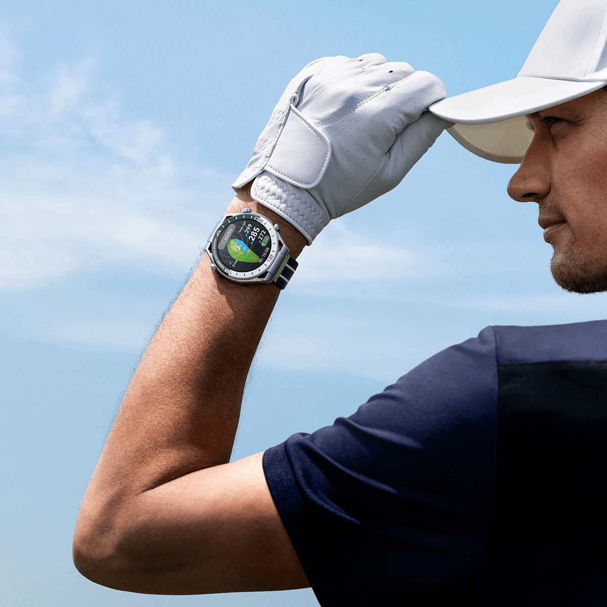 Hombre con guante de golf usando un smartwatch, mirando al cielo.