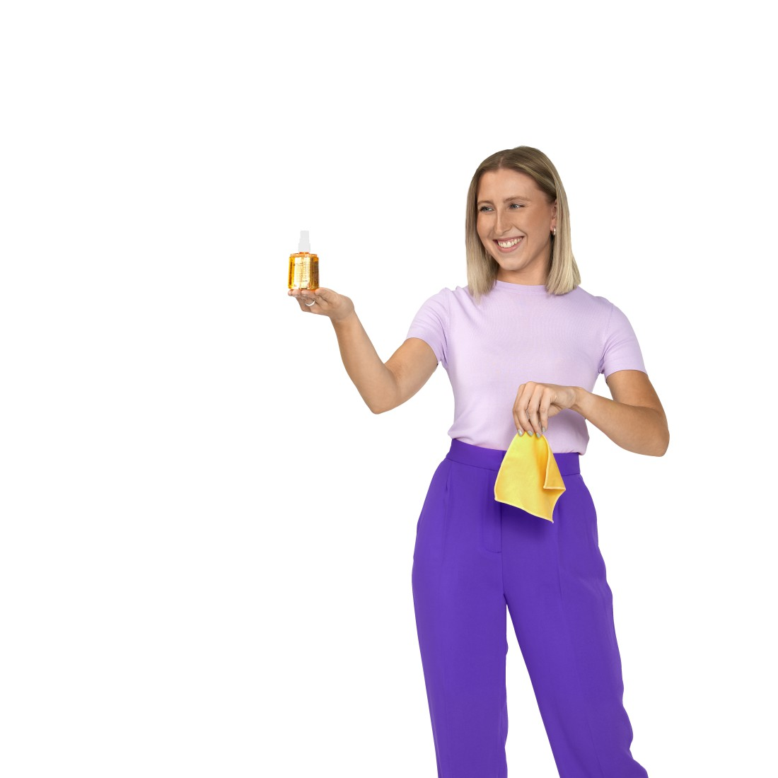 Frau hält Sprühflasche und gelbes Tuch. Trägt lila Oberteil und Hose. Weißer Hintergrund.