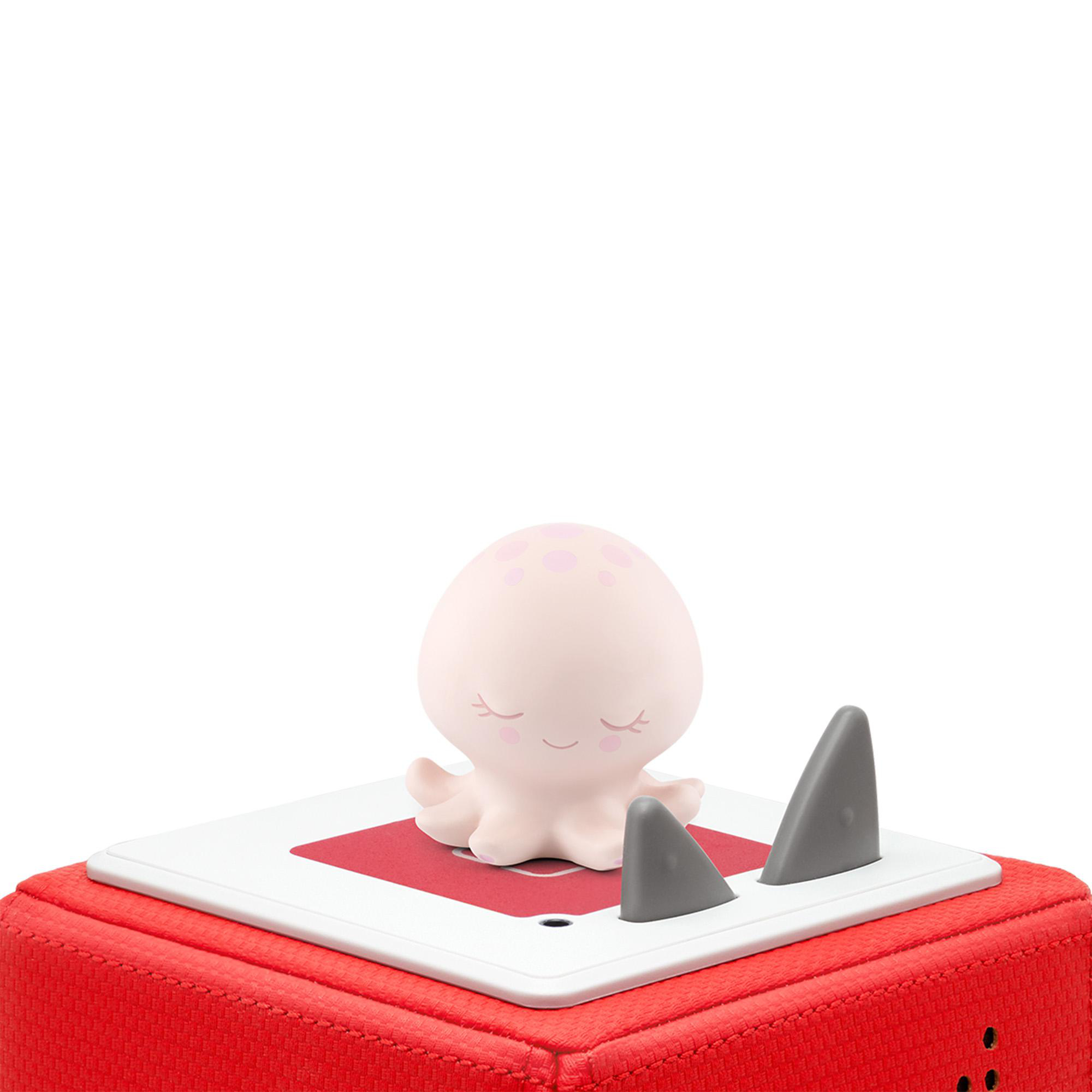 Rosa Oktopus-Spielzeug auf weißer Oberfläche. Zwei graue Haifischflossen. Rote Box unten.