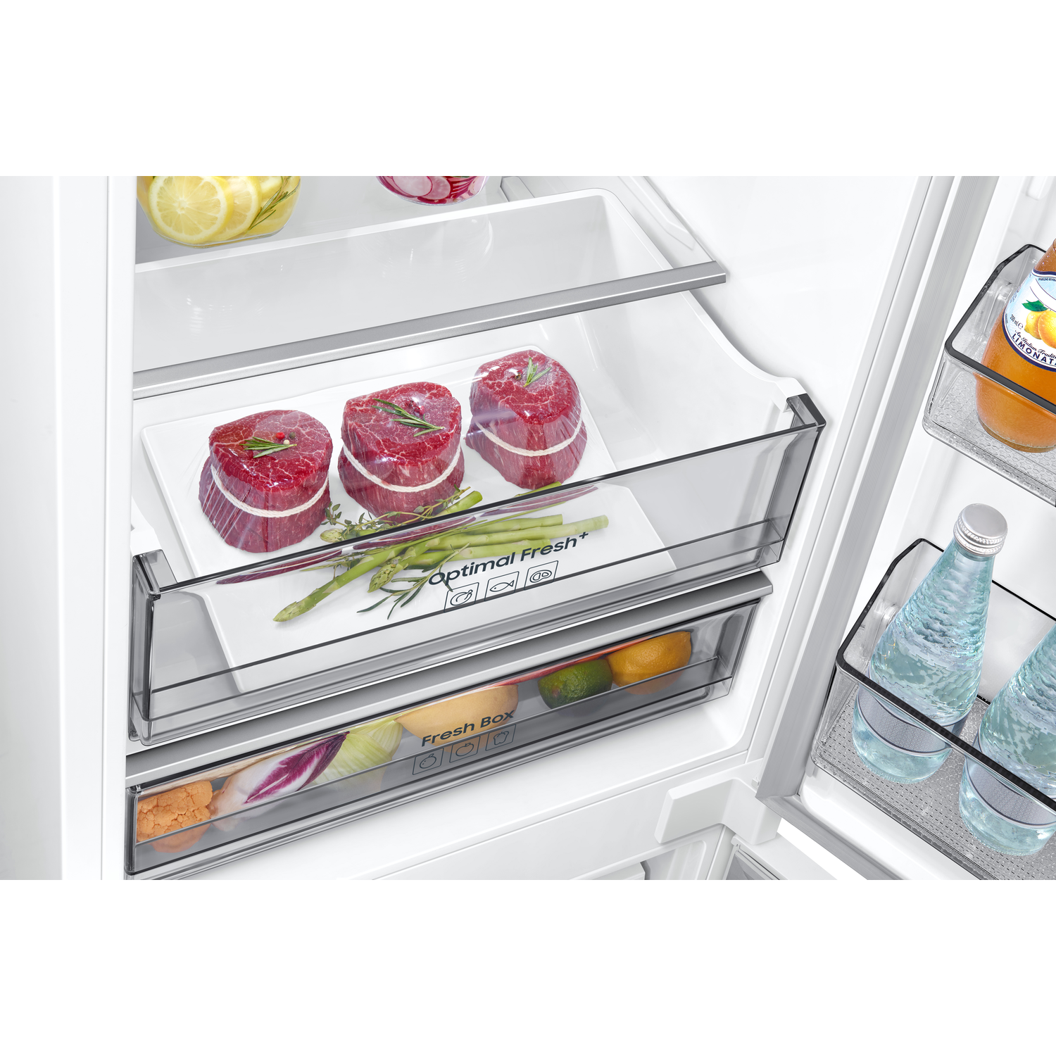 Inside a refrigerator, fresh food in drawers: meat, asparagus, and vegetables.
