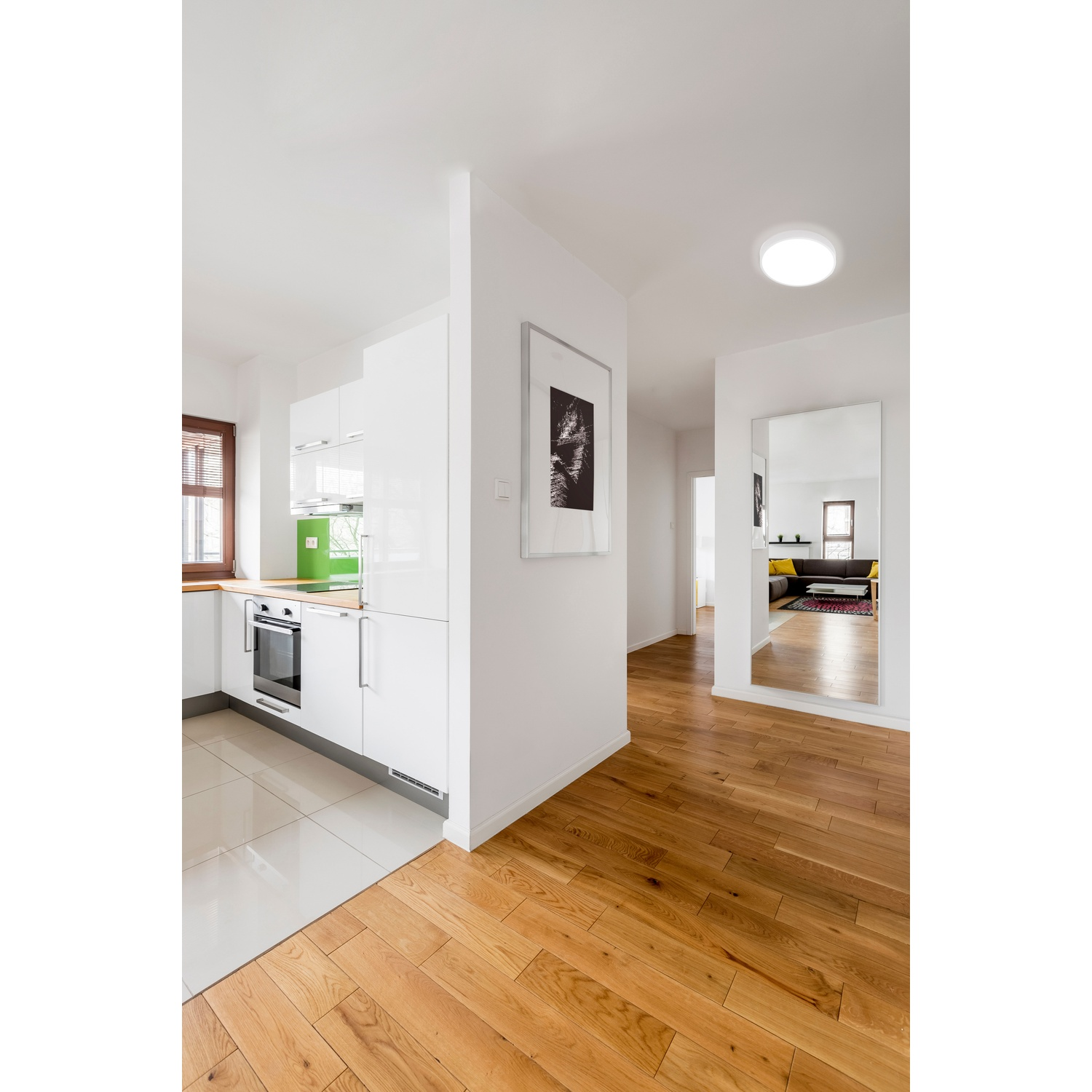Cucina moderna con mobili bianchi, pavimento in legno e specchio.