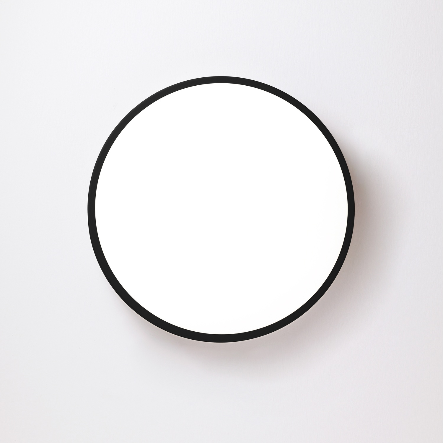 Uno specchio circolare nero con una cornice nera è su un muro bianco.