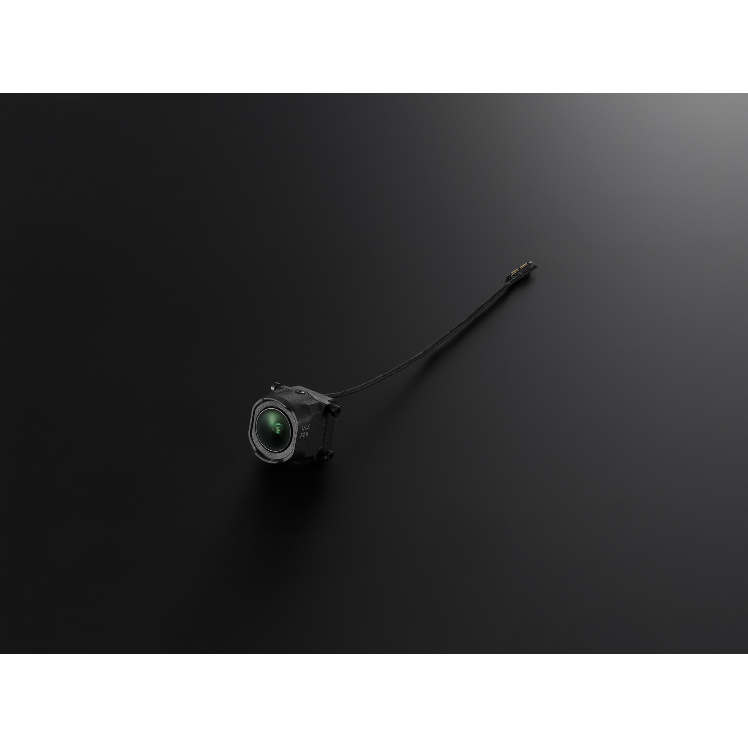 Small camera module with lens and attached wire, angled on a black surface.