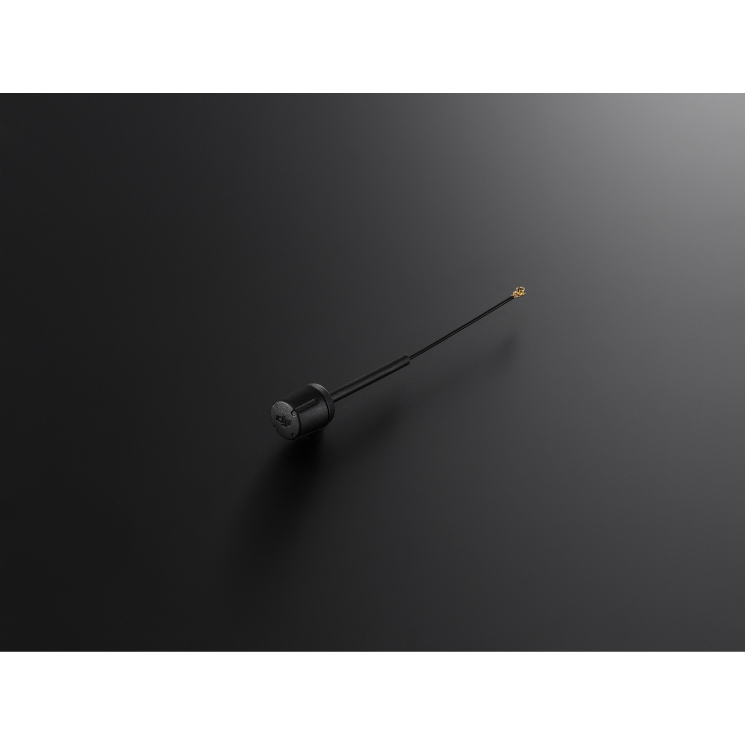 A black antenna, with a small gold tip, lying on a dark surface.