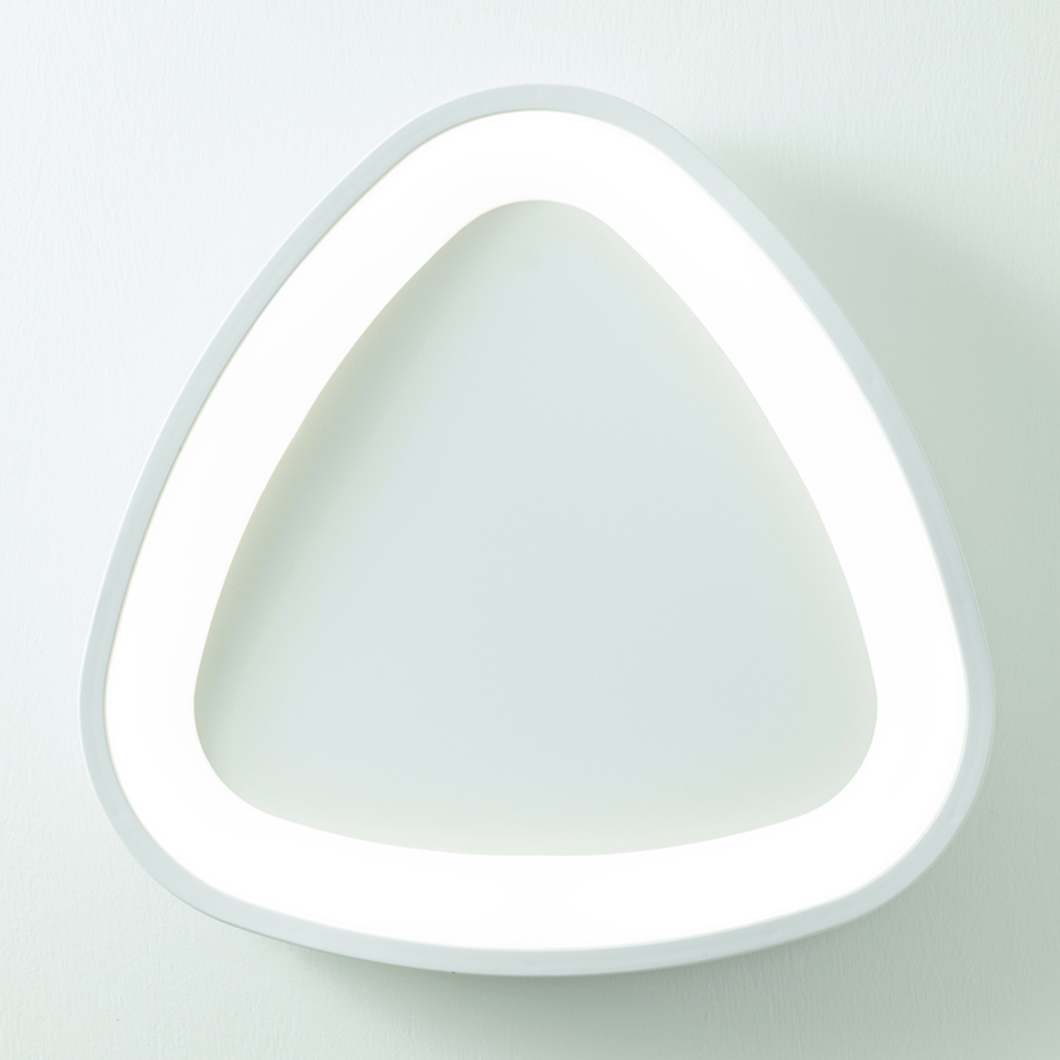 Lampada bianca a forma di triangolo su un muro bianco. La luce è accesa.