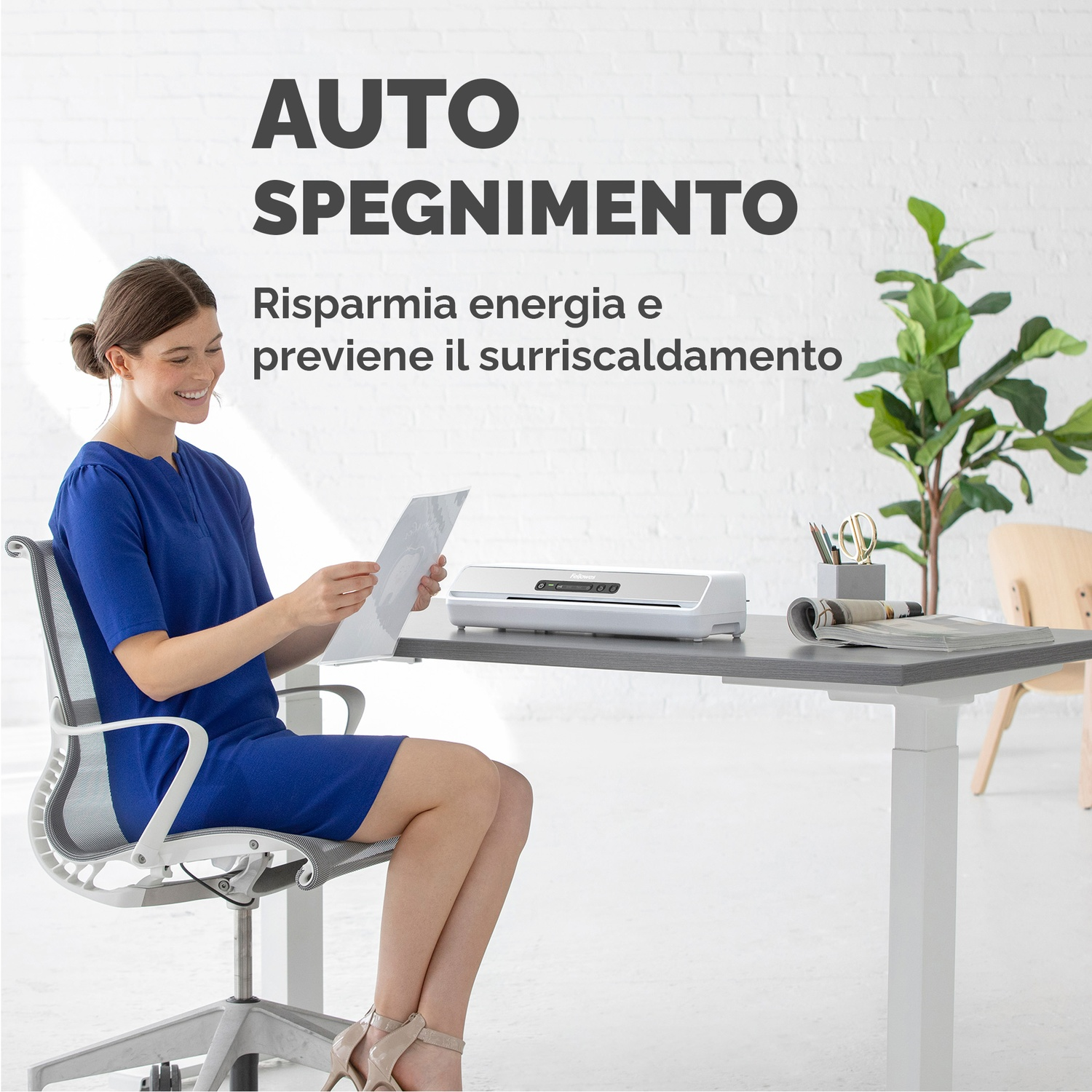 Una donna è seduta a una scrivania, tiene in mano un documento, con una plastificatrice sulla scrivania.