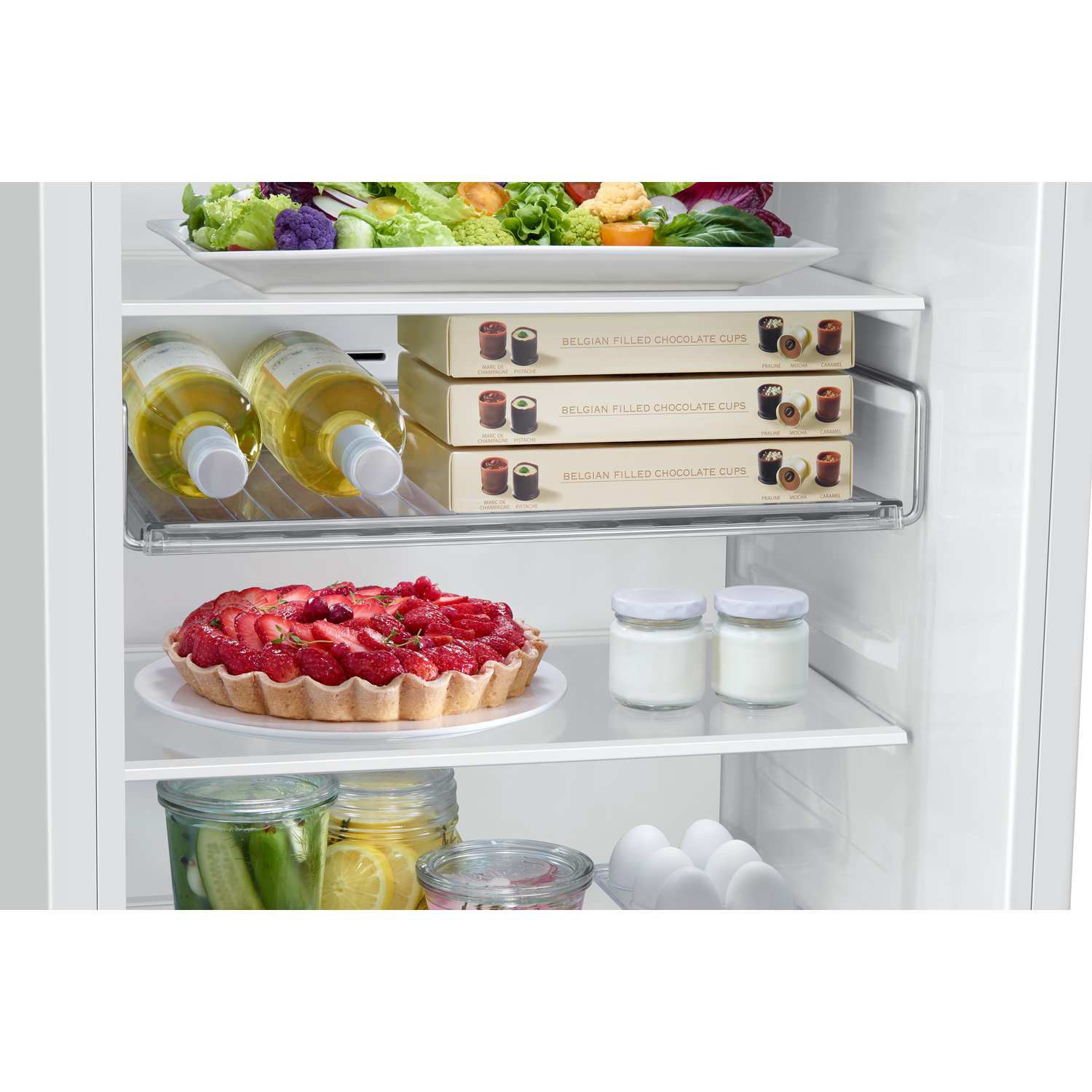 Inside a fridge: vegetables, filled chocolate cups, a tart and jars.