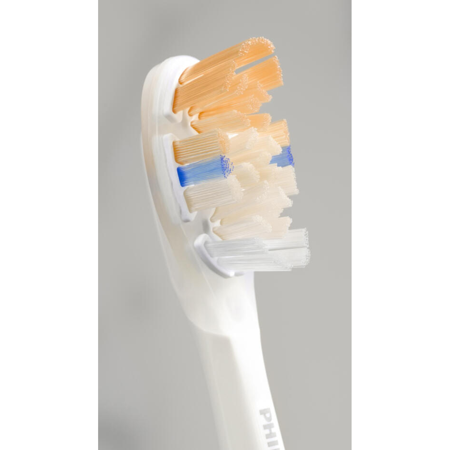 Close-up of a toothbrush head. Orange, blue and white bristles.