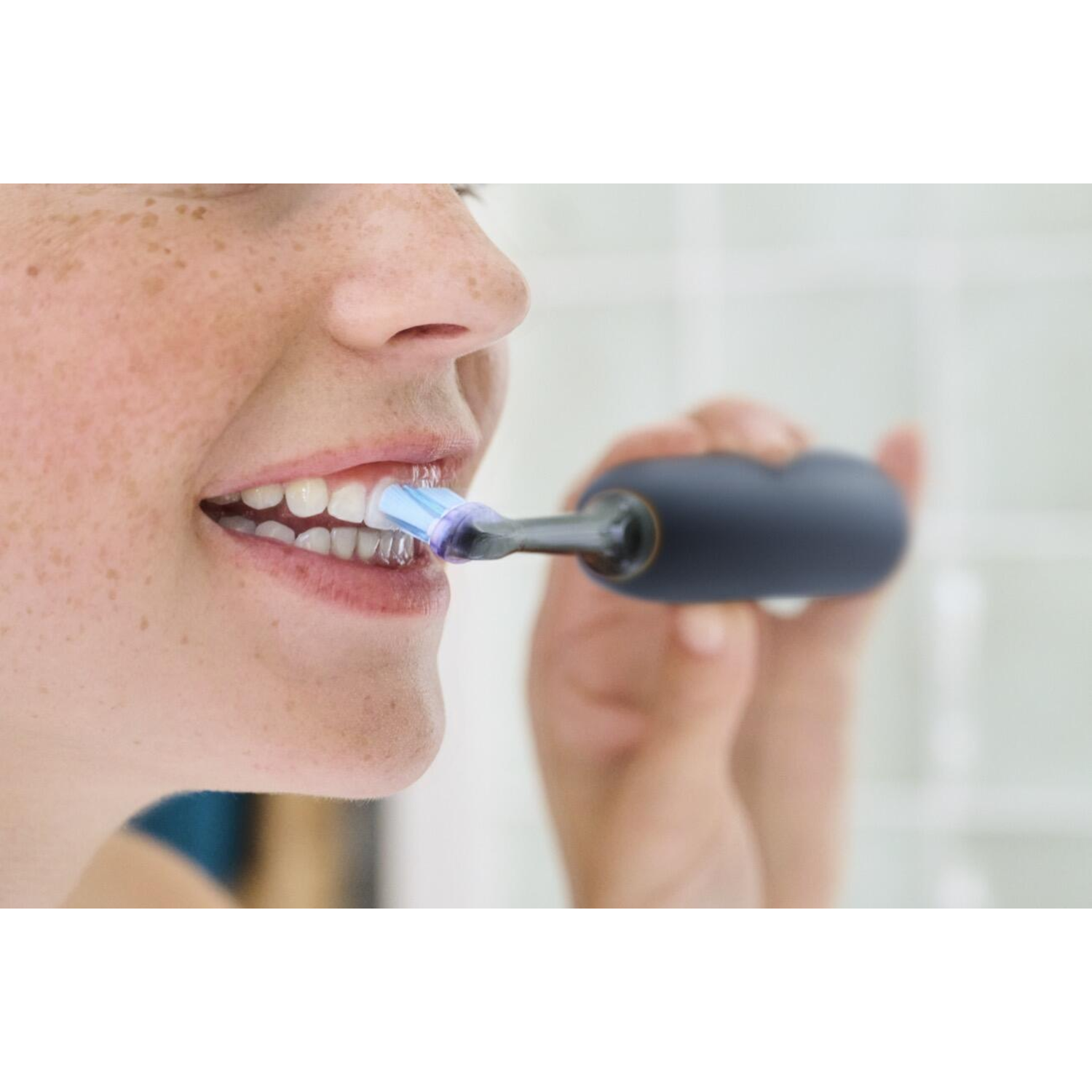 Woman brushing teeth with a dark blue electric toothbrush.