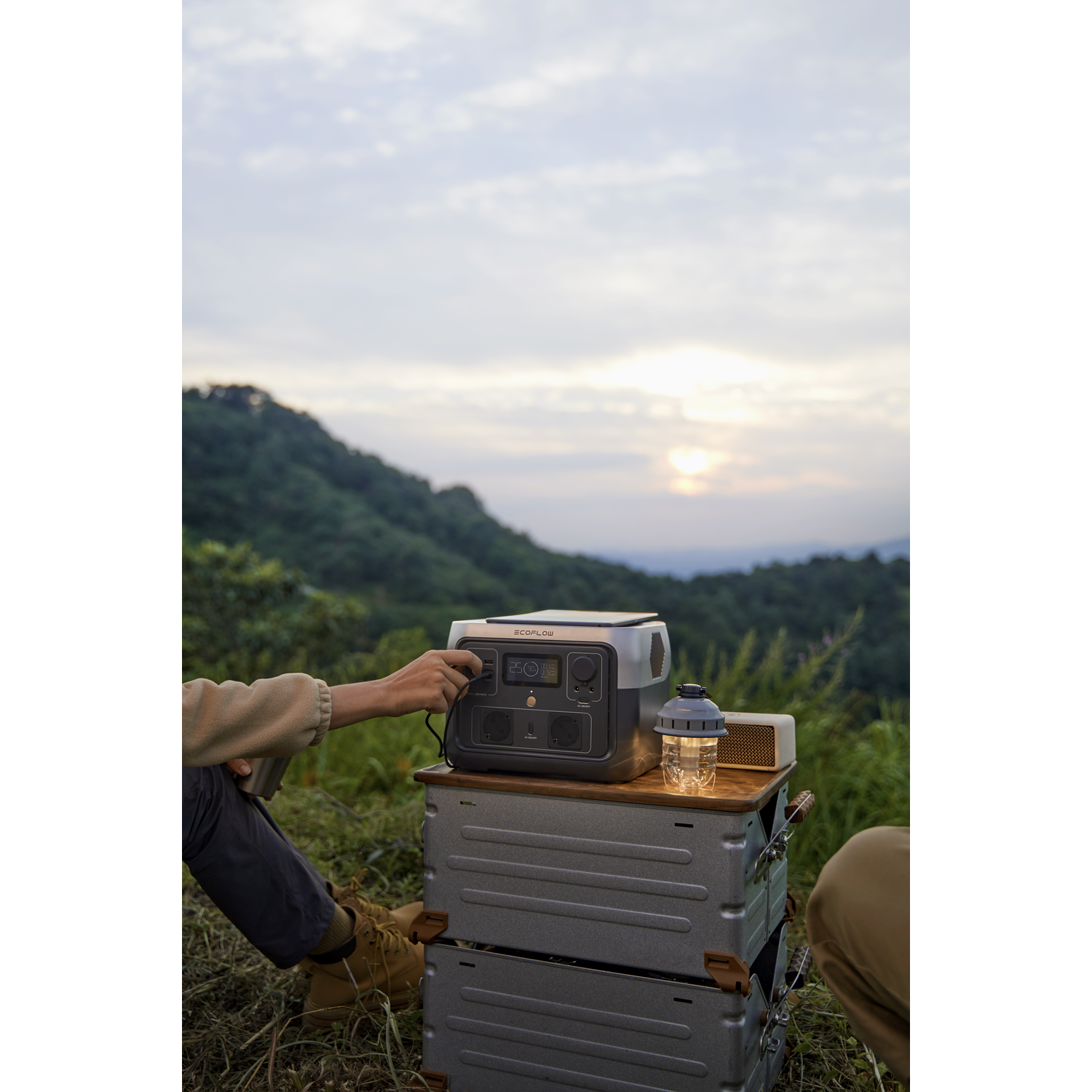 Person using a power station on a wooden table in a natural setting.