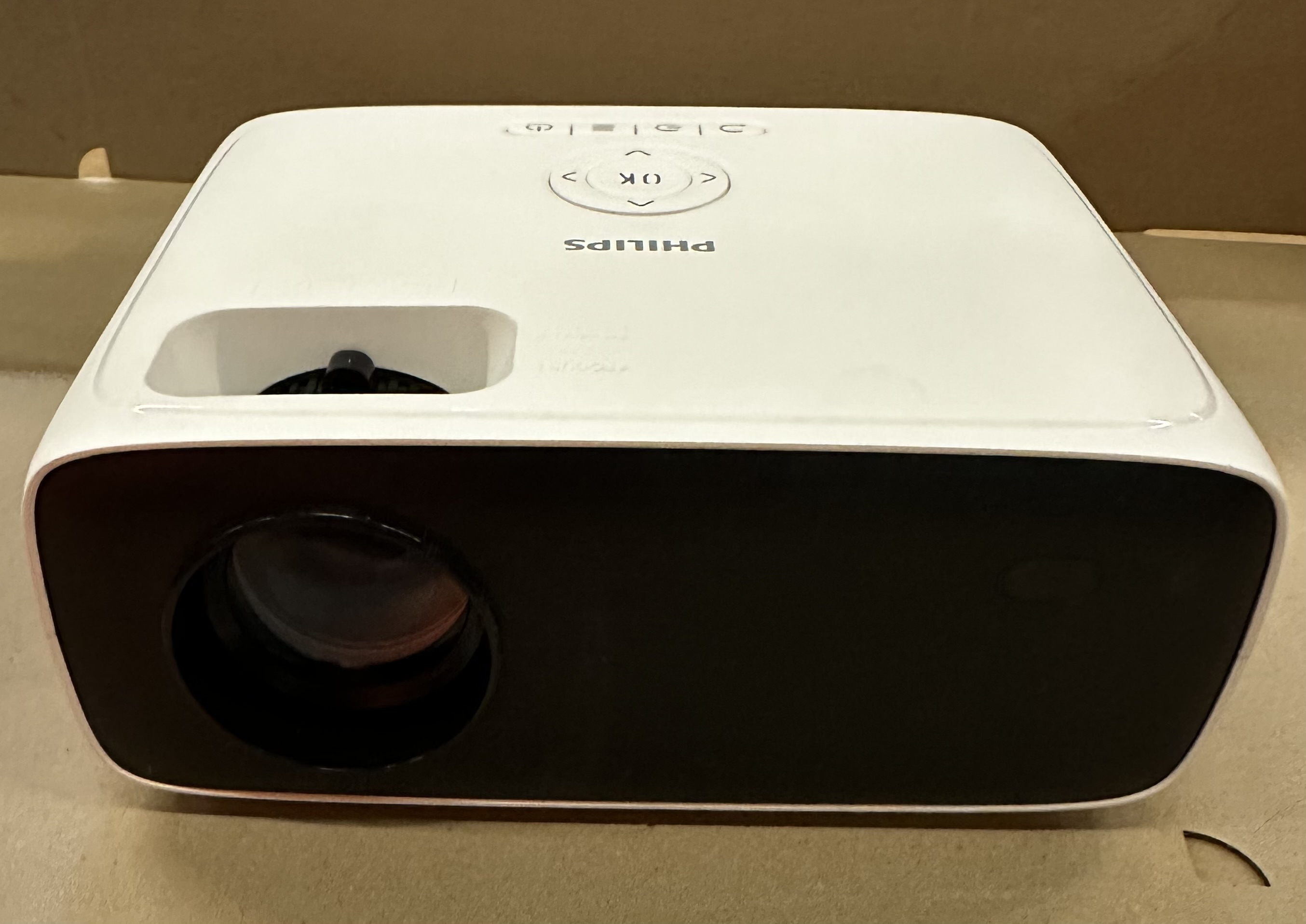 Biały projektor Philips z czarnym obiektywem. Przyciski sterowania na górze.