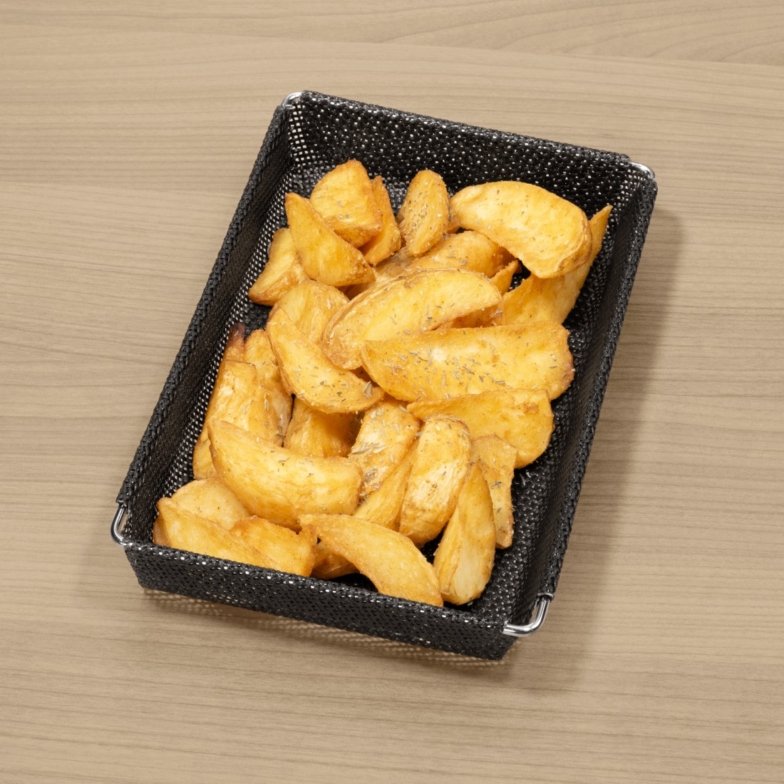 Frittierte Kartoffelspalten in einem schwarzen Drahtgitterkorb auf Holz.