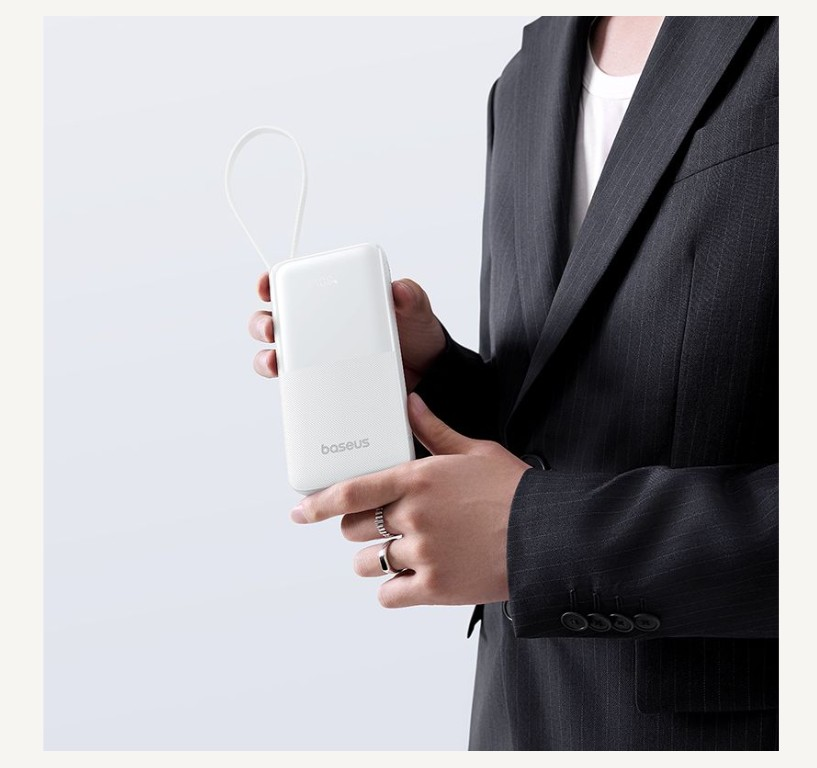 Kişi beyaz Baseus powerbank tutuyor, takım elbise giyiyor.