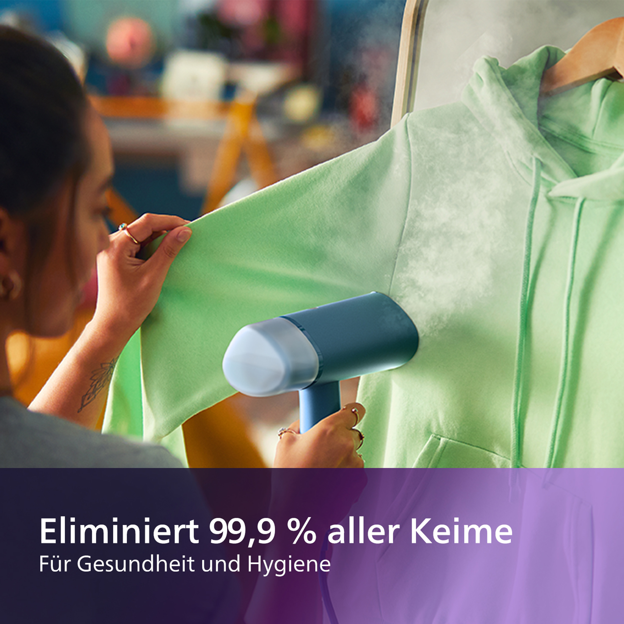 Eine Frau, die einen grünen Kapuzenpullover dämpft. Text: 'Eliminiert 99,9 % aller Keime'.