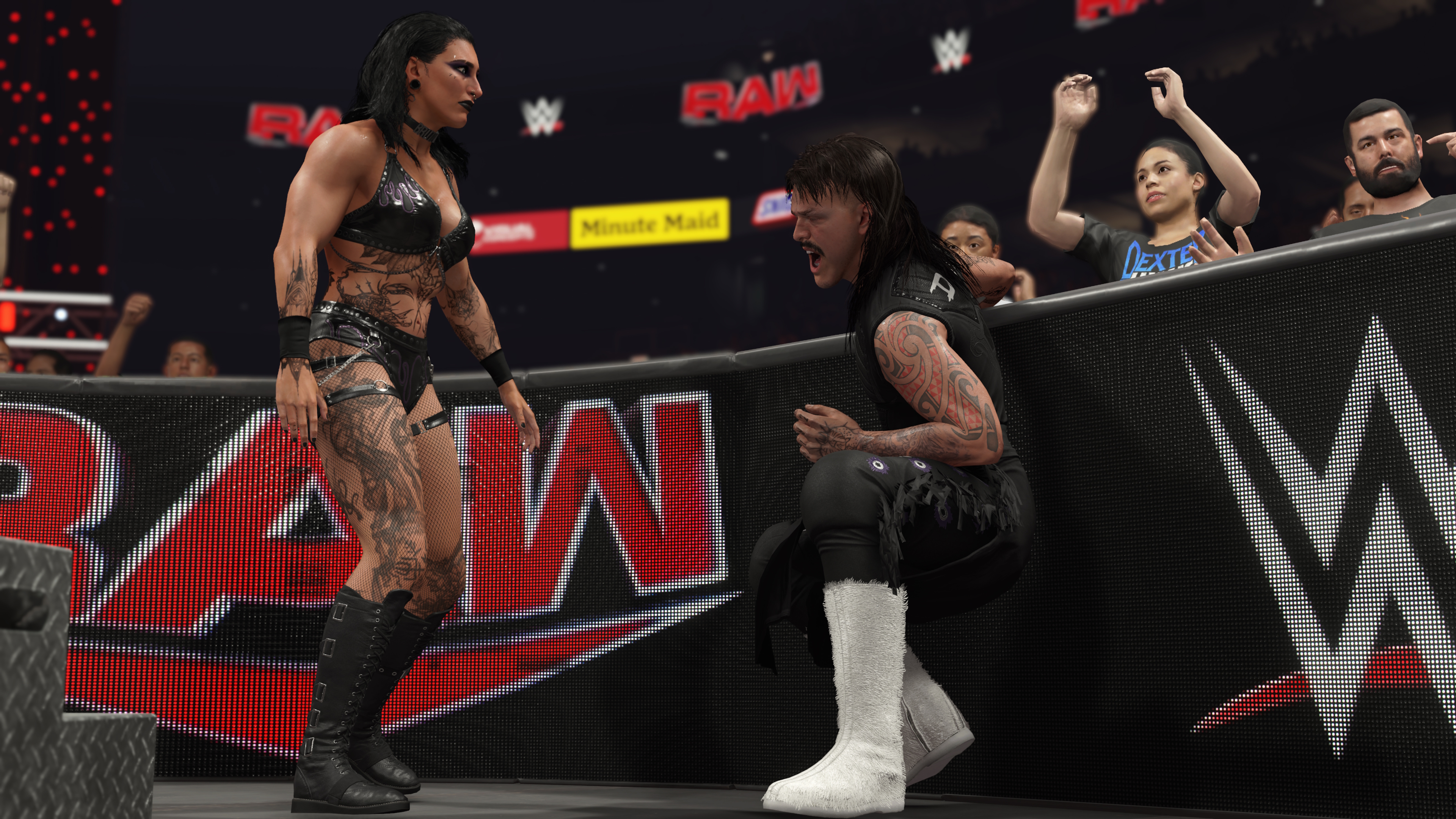 Wrestler in einem Ring, eine Wrestlerin steht einem anderen gegenüber, mit Publikum im Hintergrund.