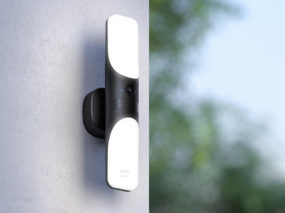 Czarna zewnętrzna lampa bezpieczeństwa na ścianie, z rozmytym zielonym tłem.