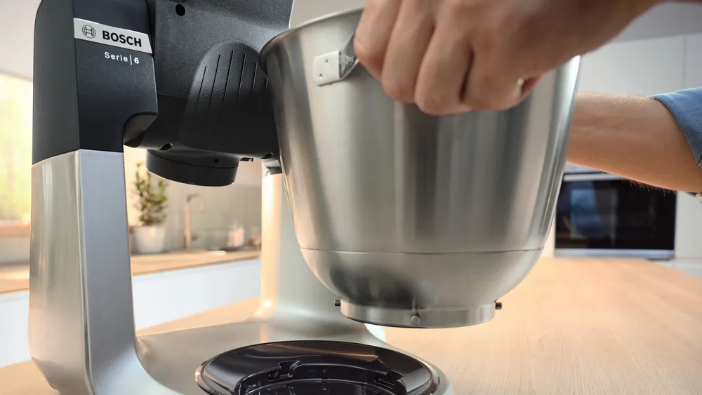 Egy Bosch robotgép rozsdamentes acéltartóval, amelyet egy kéz tart.