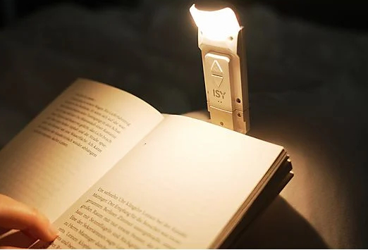 Książka z małą białą lampką na klips. Światło oświetla stronę.