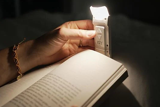 Ręka trzyma książkę z lampką do czytania na klips. Światło jest na stronie.