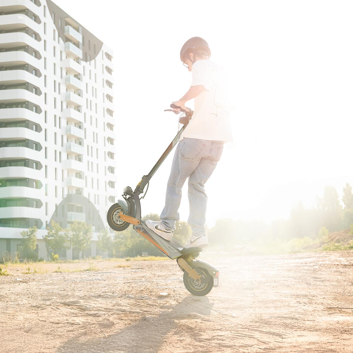 Persona en patinete eléctrico haciendo caballito. Fondo de ciudad.