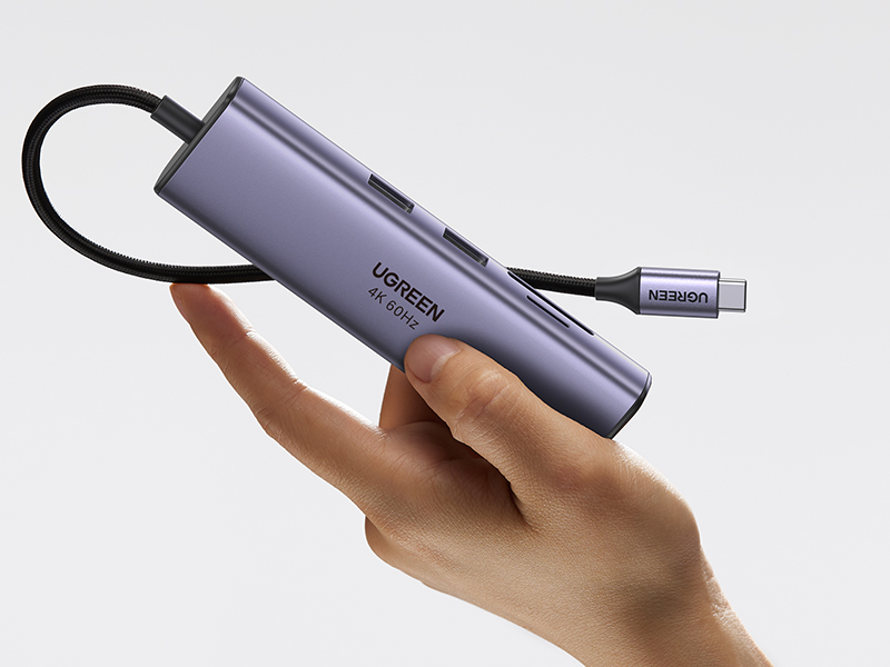 Bir el, mor bir UGREEN USB-C hub'ını tutuyor. Birkaç bağlantı noktası ve bağlı bir kablosu var.