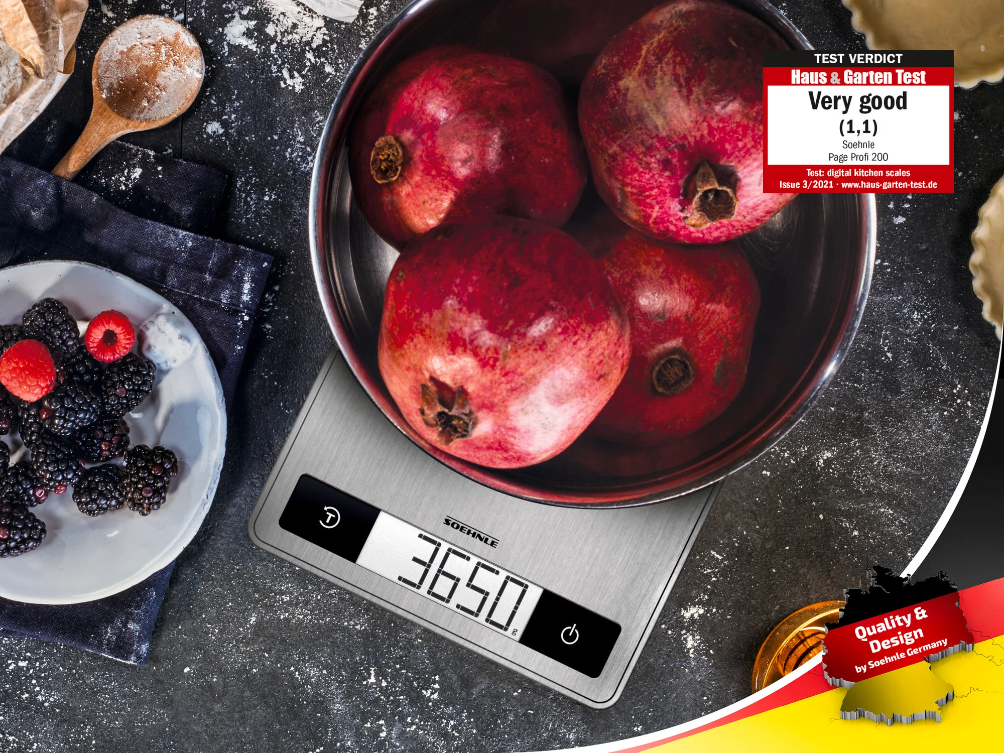 Eine silberne Waage mit einer Schüssel mit Granatäpfeln und einem Teller mit Brombeeren auf schwarzem Untergrund.
