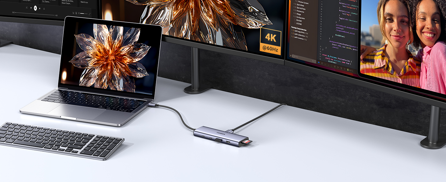 Beyaz bir masada iki monitöre, bir klavyeye ve bir yuvaya bağlı dizüstü bilgisayar. 4K ekran görünür.