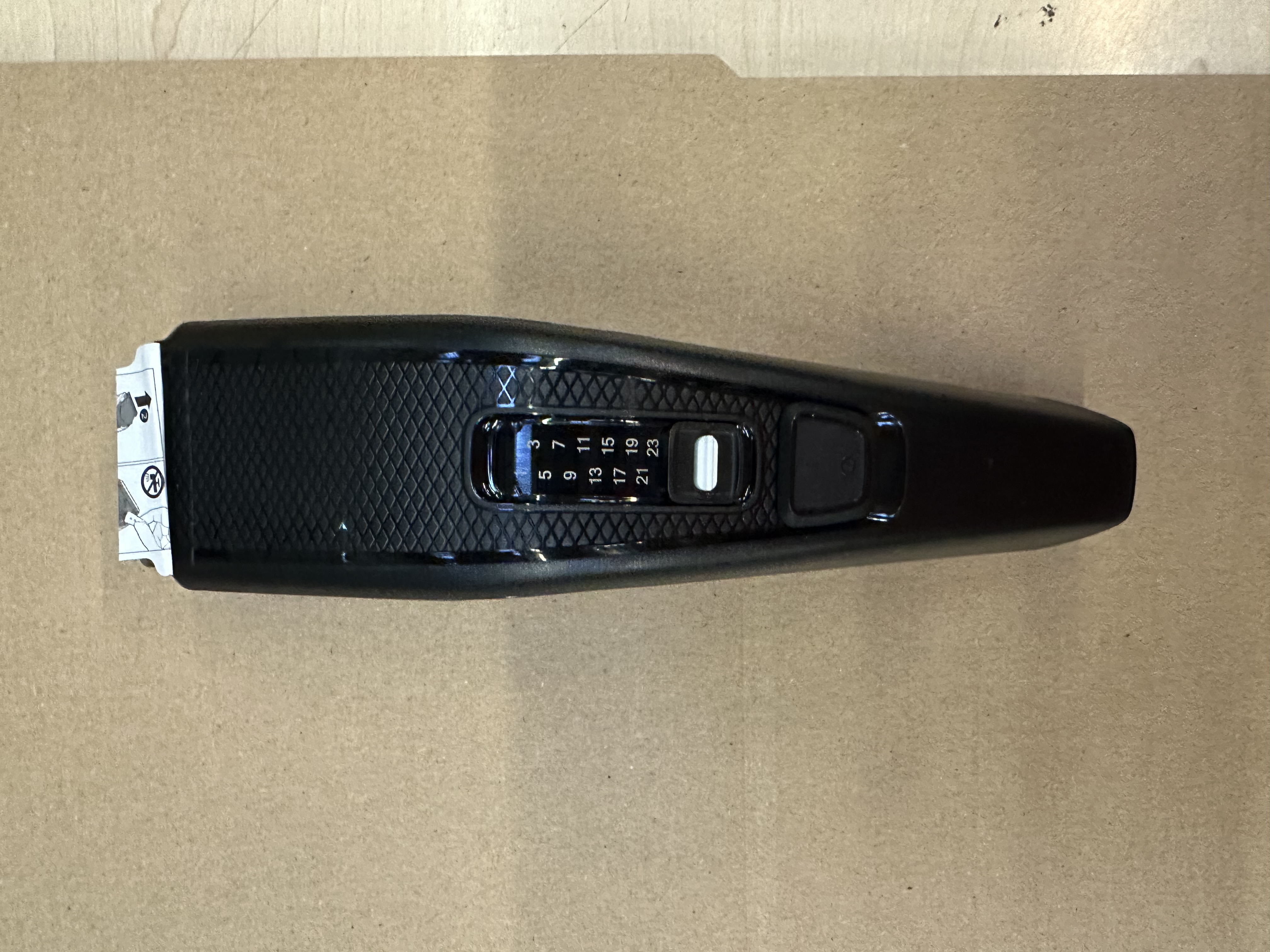 Czarna maszynka do strzyżenia brody widziana z góry na brązowej powierzchni.