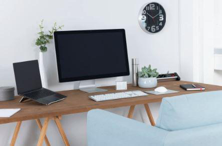 Arbeitsplatz mit Laptop, Desktop-Monitor, Tastatur und Uhr.
