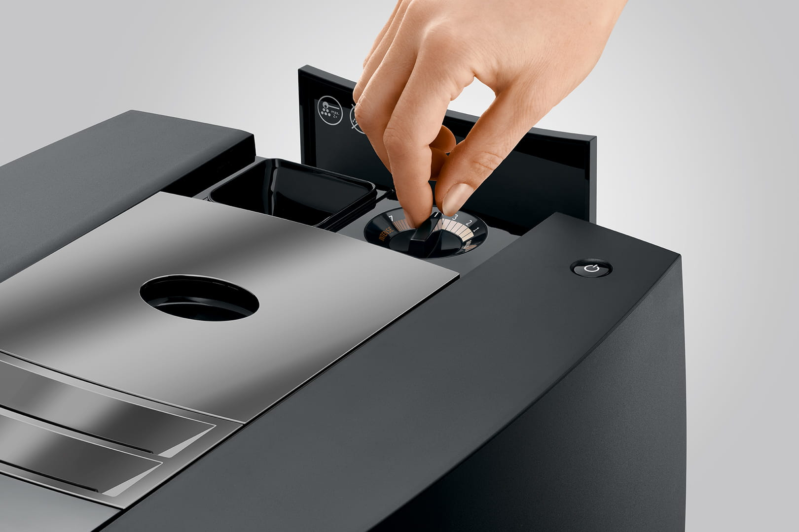 Dłoń osoby regulująca pokrętło na czarnym ekspresie do kawy.