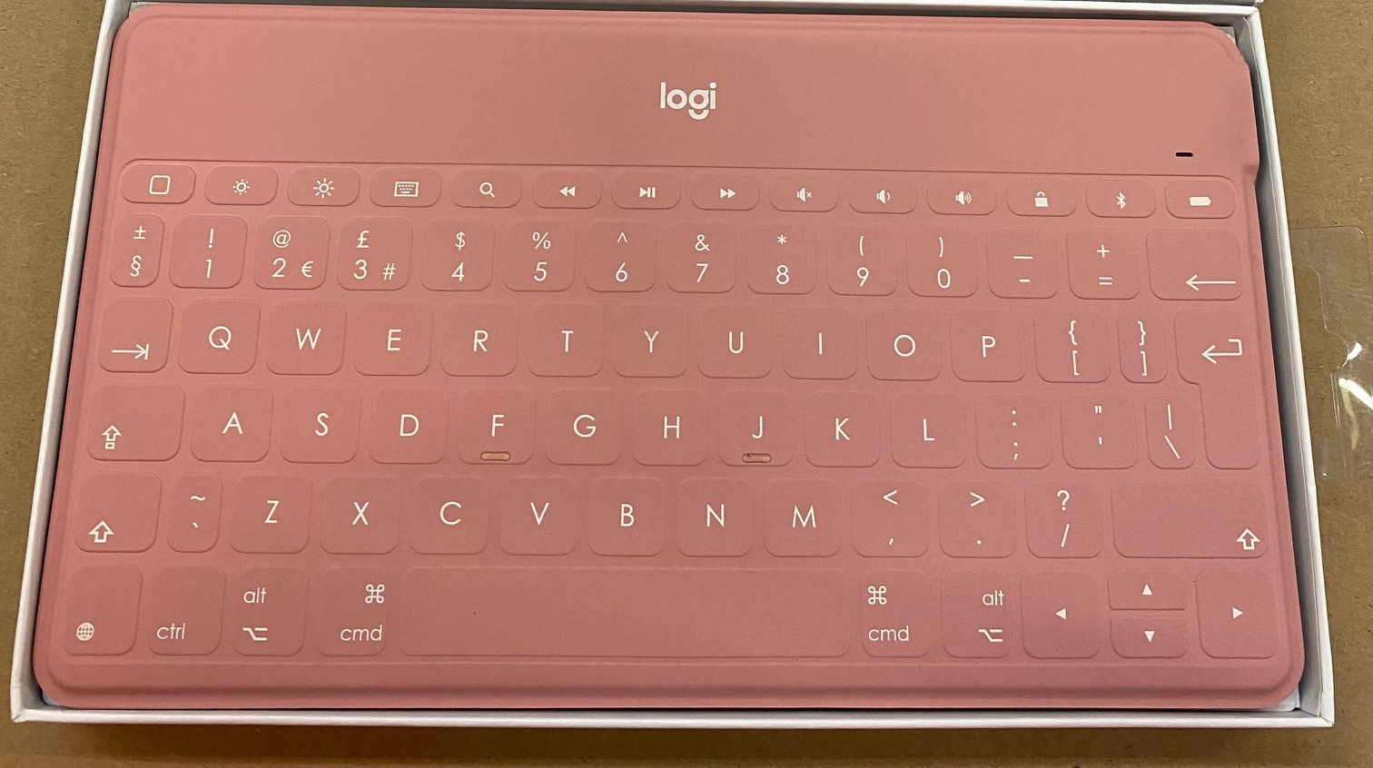 Różowa klawiatura, widok z góry, z klawiszami i symbolami. Białe tło, marka Logitech.