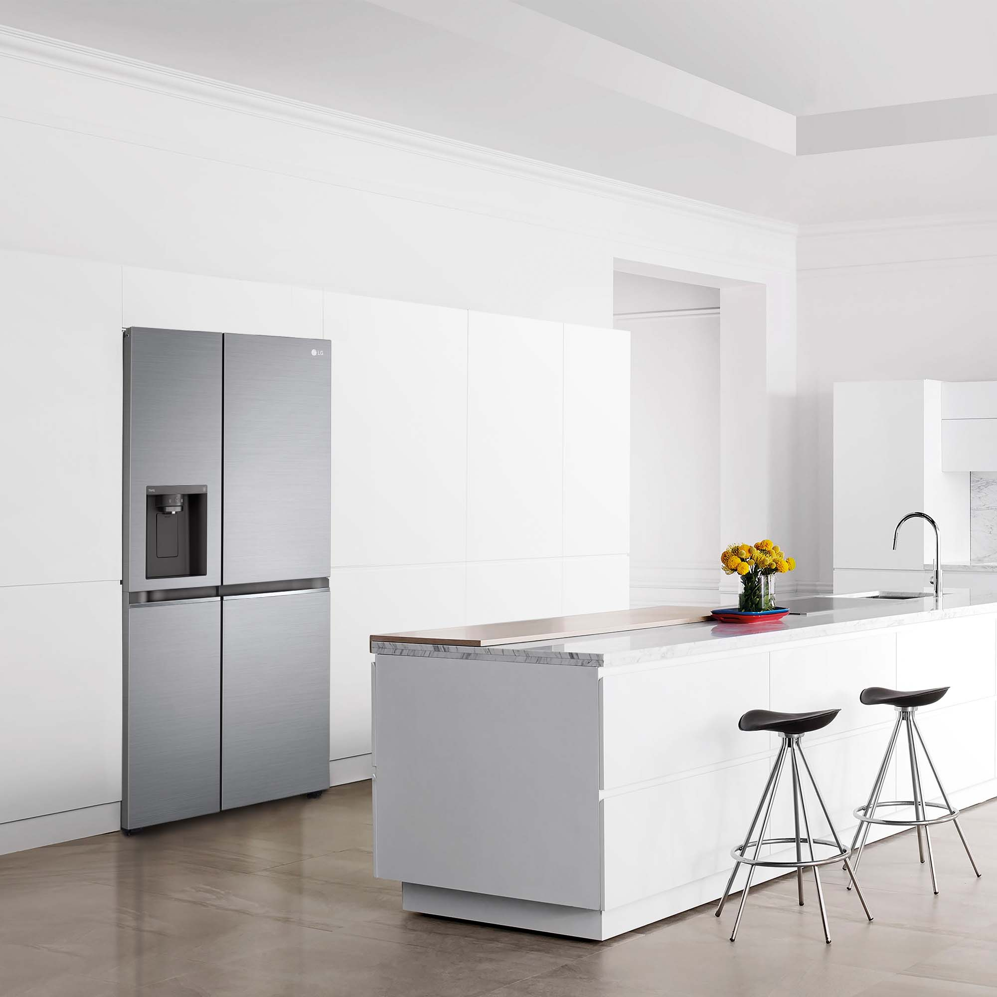 Cocina moderna con refrigerador plateado, encimeras blancas y taburetes.