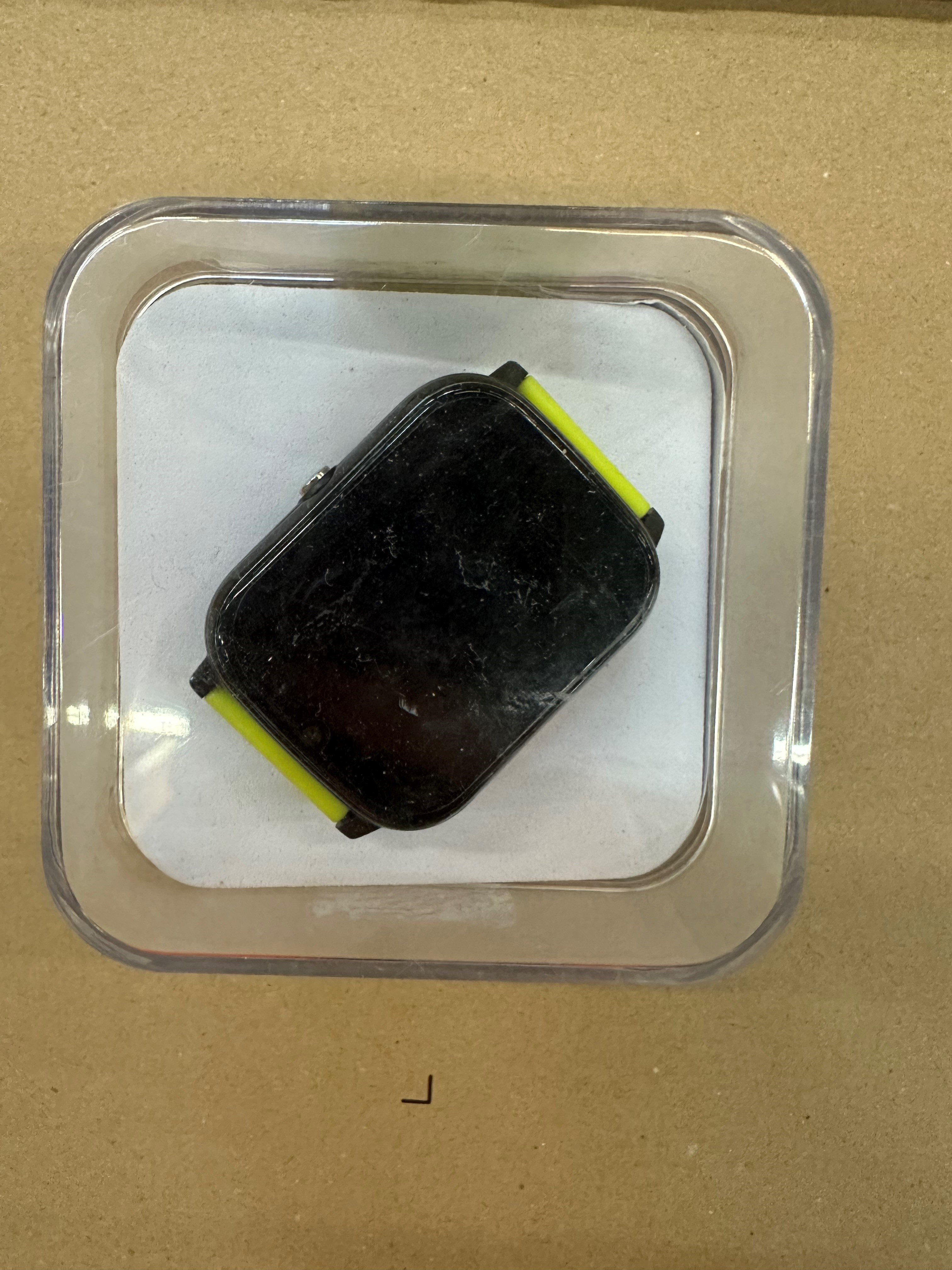 Czarny smartwatch z neonowożółtymi akcentami w przezroczystym pojemniku.