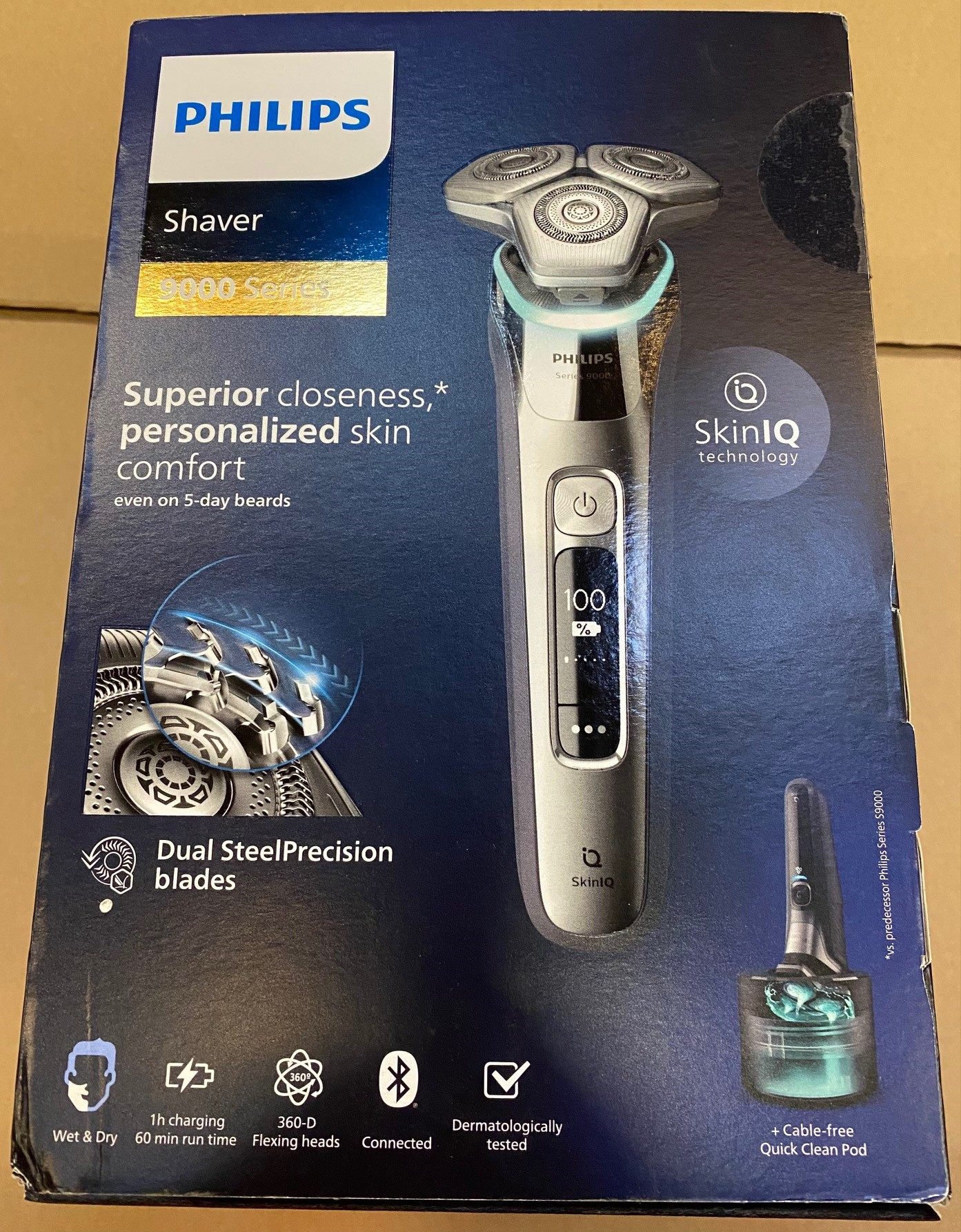 Pudełko golarki Philips z golarką i jej częściami. Pudełko znajduje się na brązowej powierzchni.