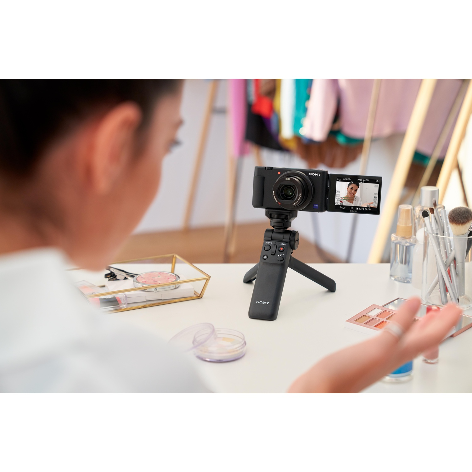Una donna si filma con una piccola fotocamera su un treppiede, circondata da trucco e accessori.