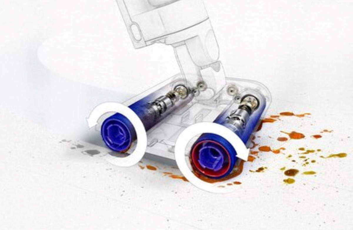 Głowica odkurzacza z wirującymi niebieskimi i czerwonymi wałkami i widocznymi smugami wody.