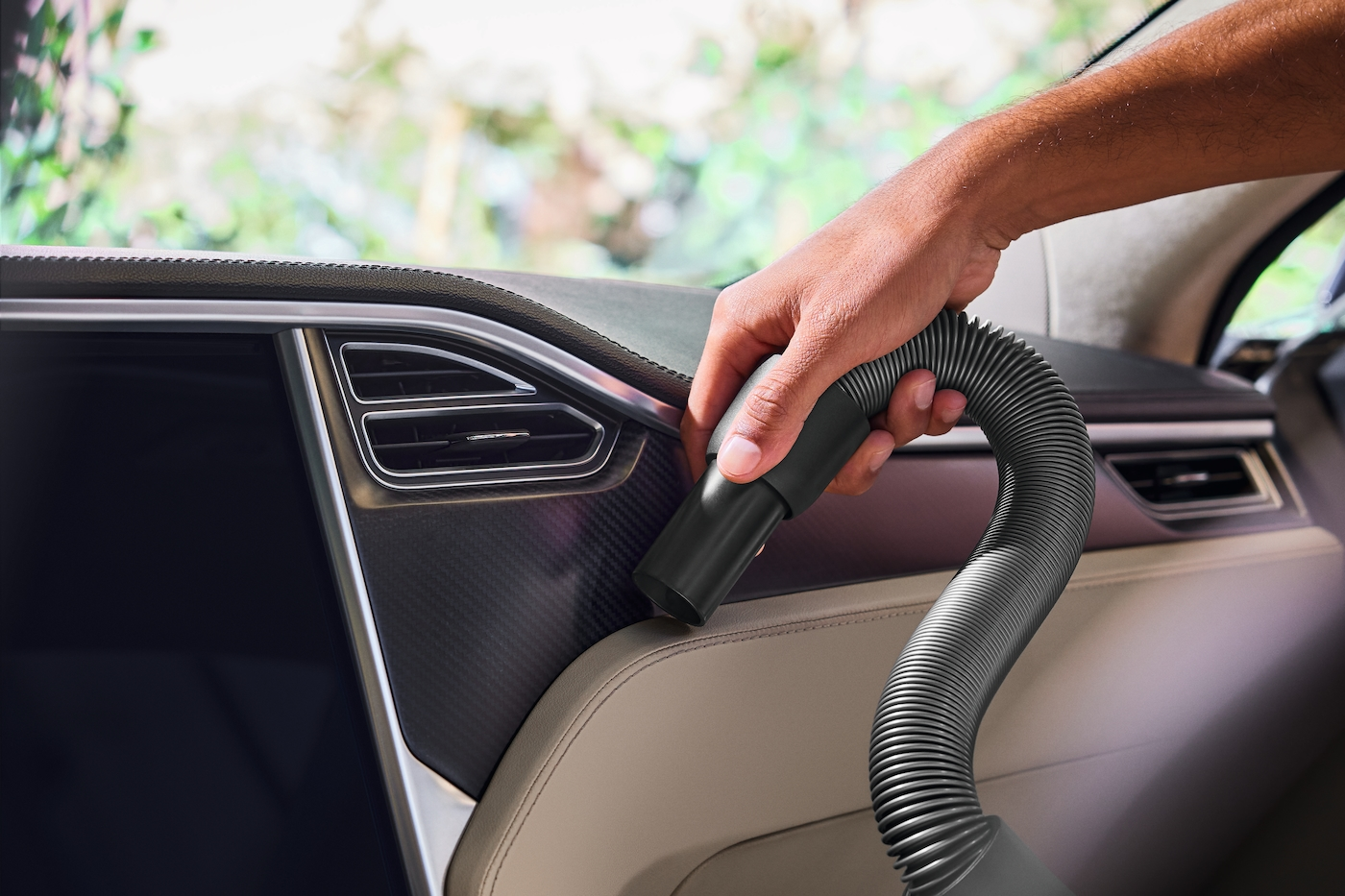 Eine Person reinigt das Armaturenbrett eines Autos mit einem Staubsauger.
